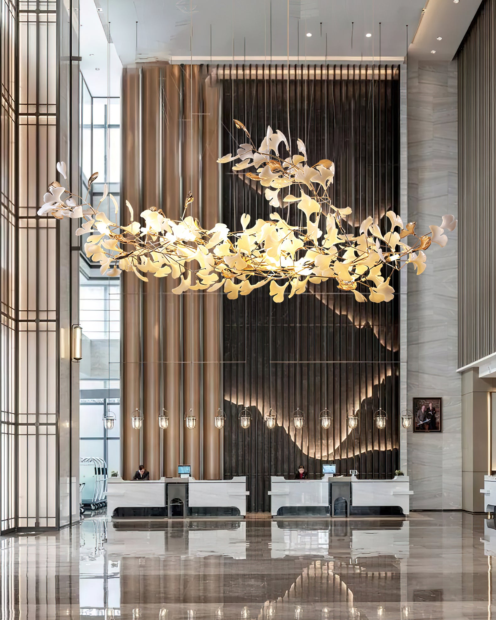 Wide tall reception hall with upward-sweeping leaf chandelier, marble desk and reflections in polished floor