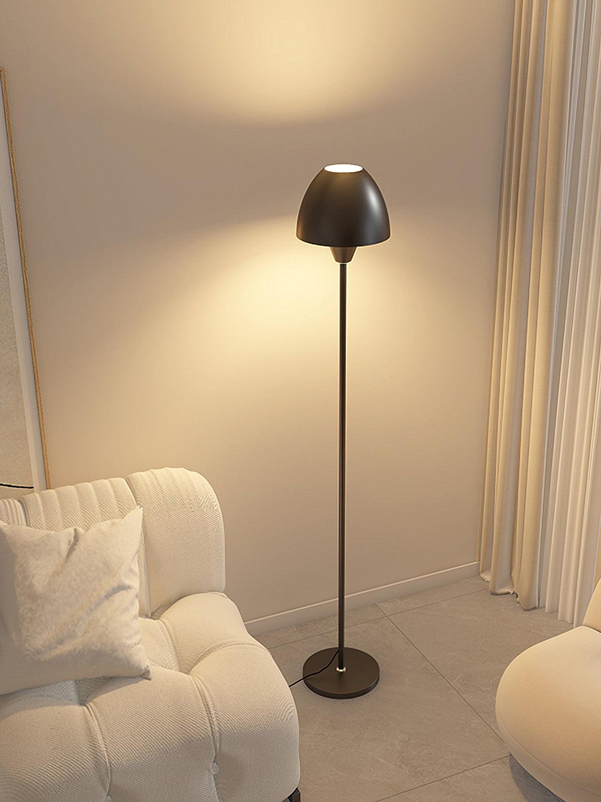 Black floor lamp between pale seats near curtains, showing the lit top opening and a cord beside the circular base