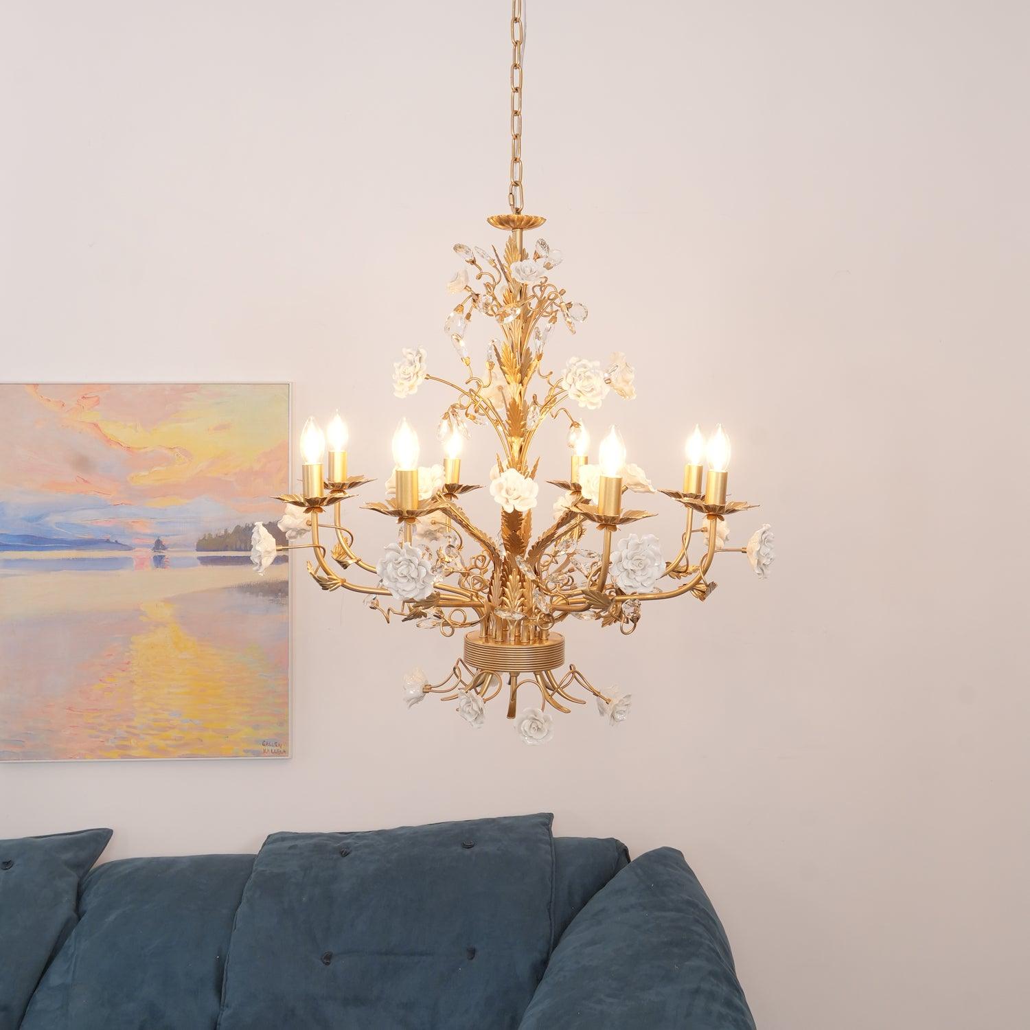 Wide view of lit floral chandelier with long chain above a blue tufted sofa, with a pastel landscape on the wall