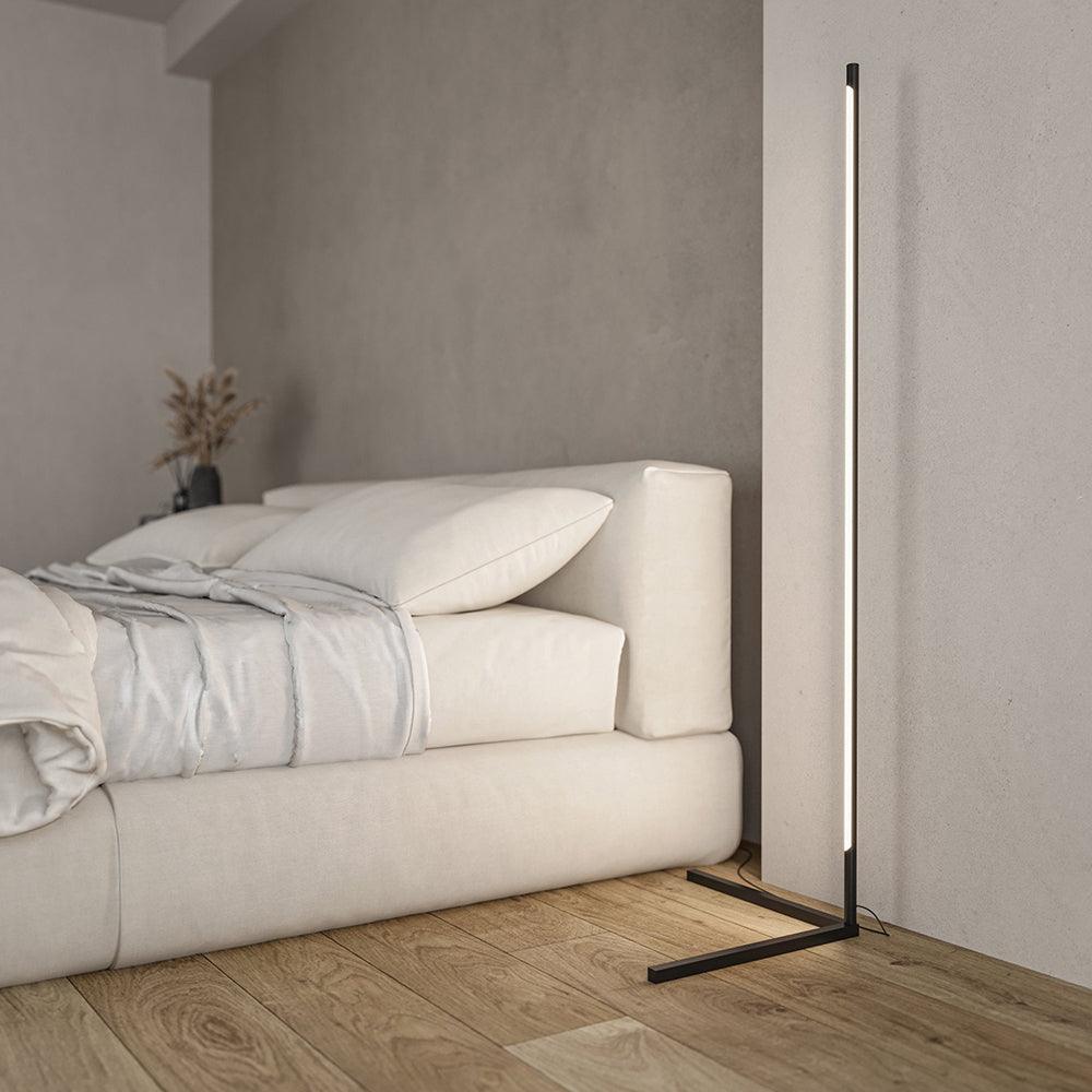 Black floor lamp with front-facing pale diffuser and angular feet beside a pale sofa or daybed
