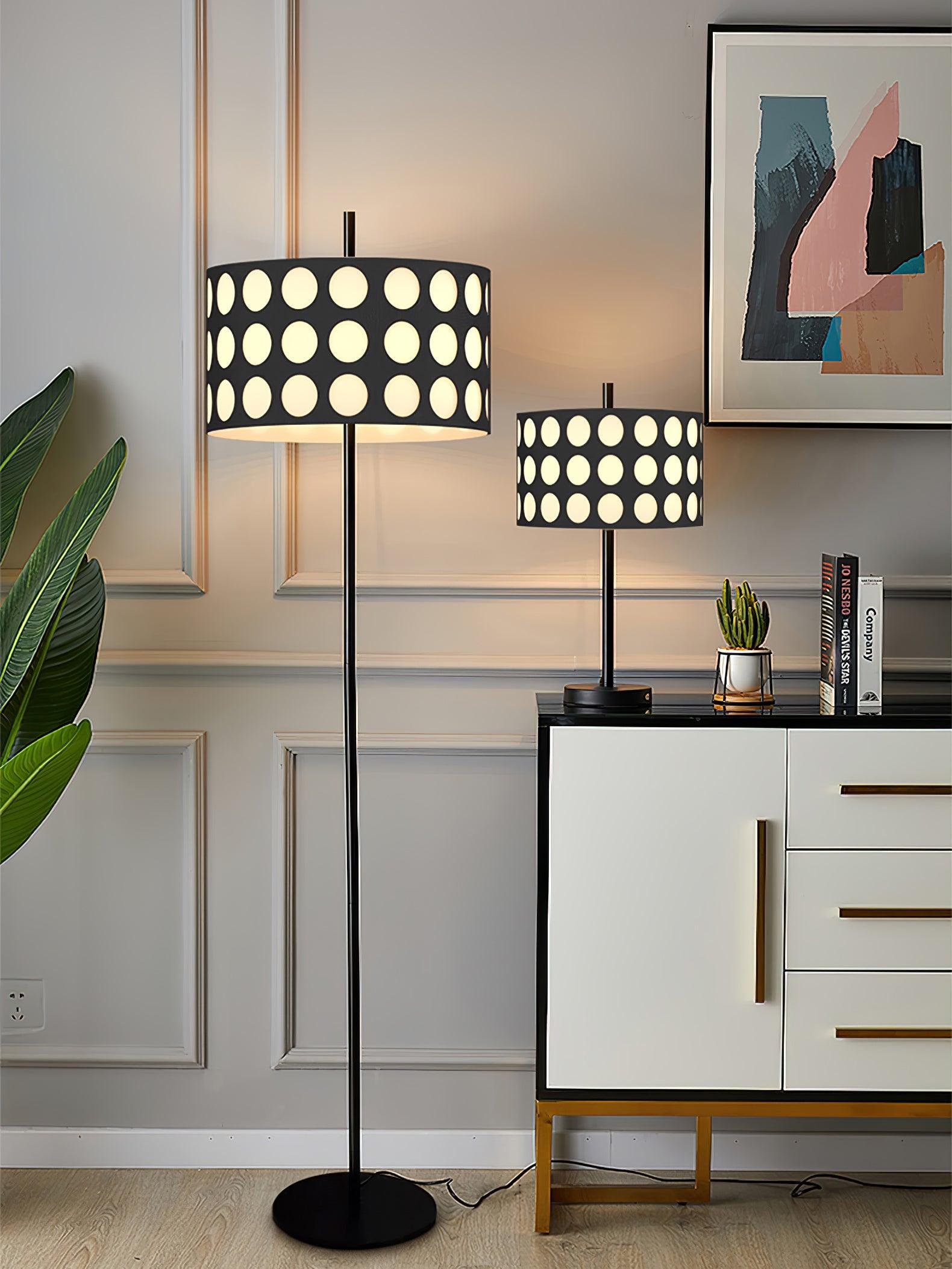 Portrait straight floor lamp and smaller table lamp with dotted drum shades beside cabinet, plant and abstract print