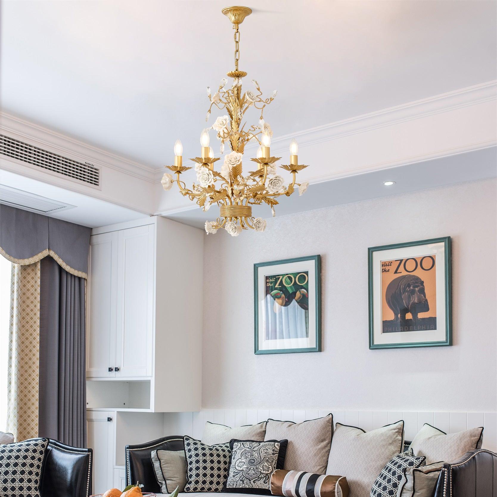 Lit gold-and-white rose chandelier above a dark sofa with pale cushions, green-framed zoo posters, white cabinets and curtains