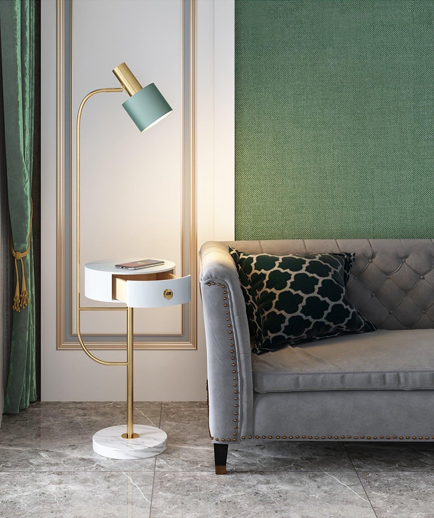 Gold Agueda lamp by green curtain and tufted gray sofa, green shade, white drawer open beneath phone and white veined base