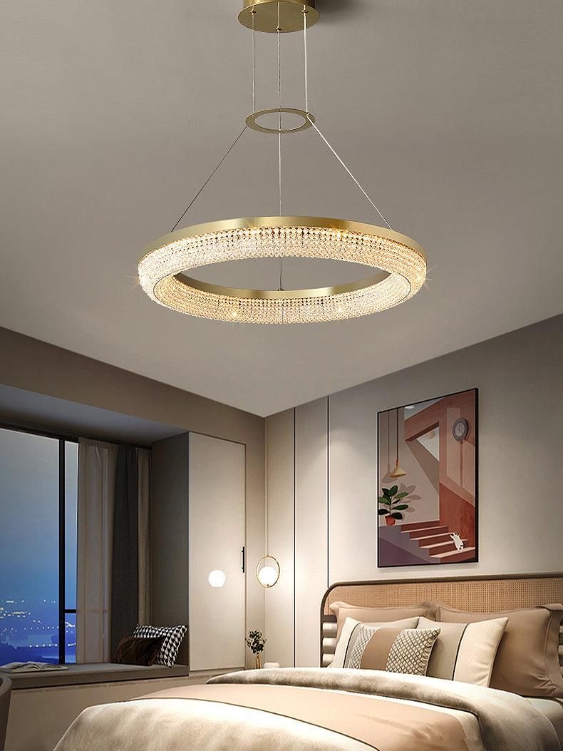 Wide bedroom view of a single crystal ring chandelier above a woven headboard and pale bedding