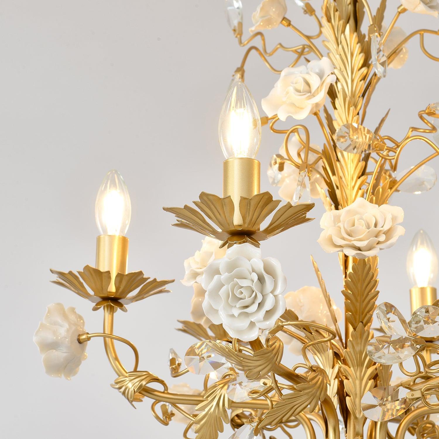 Lit candle-arm close-up with white ceramic roses, golden leaf cups and branches, and clear faceted crystal buds