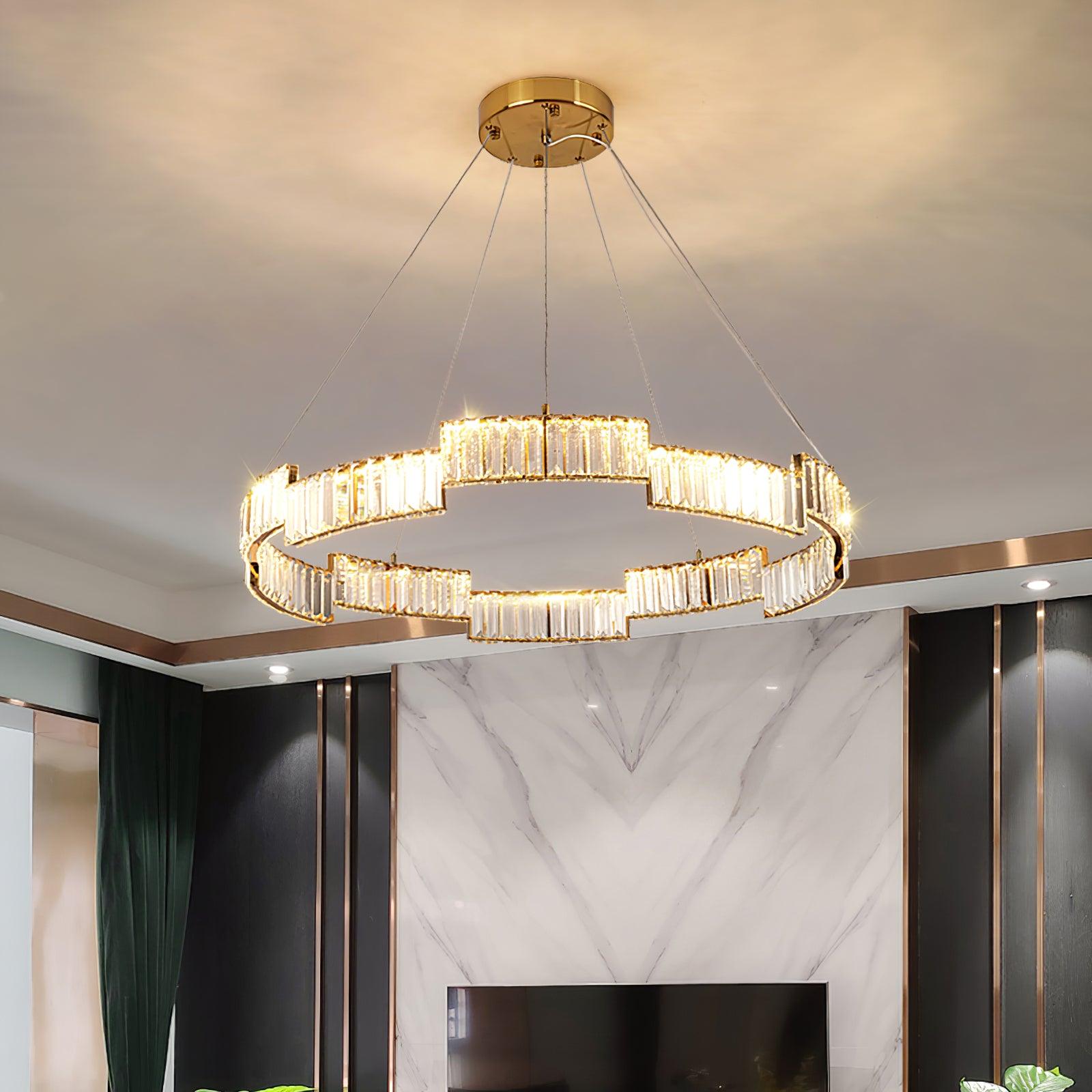 Lit stepped glass ring chandelier above a television room with veined white wall, black panels, gold trims and green curtain