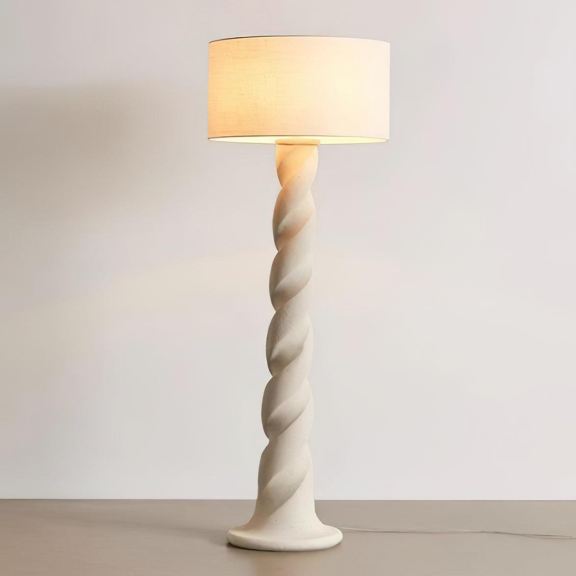 Complete lit Yisi North Tower spiral column and drum shade on grey floor against pale wall, with cord trailing right