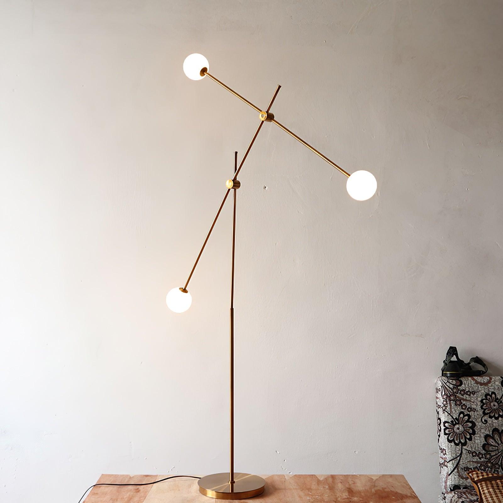 Lit Kemi lamp against a pale wall on a wooden surface, with three glowing globes, angled gold arms and a black cord