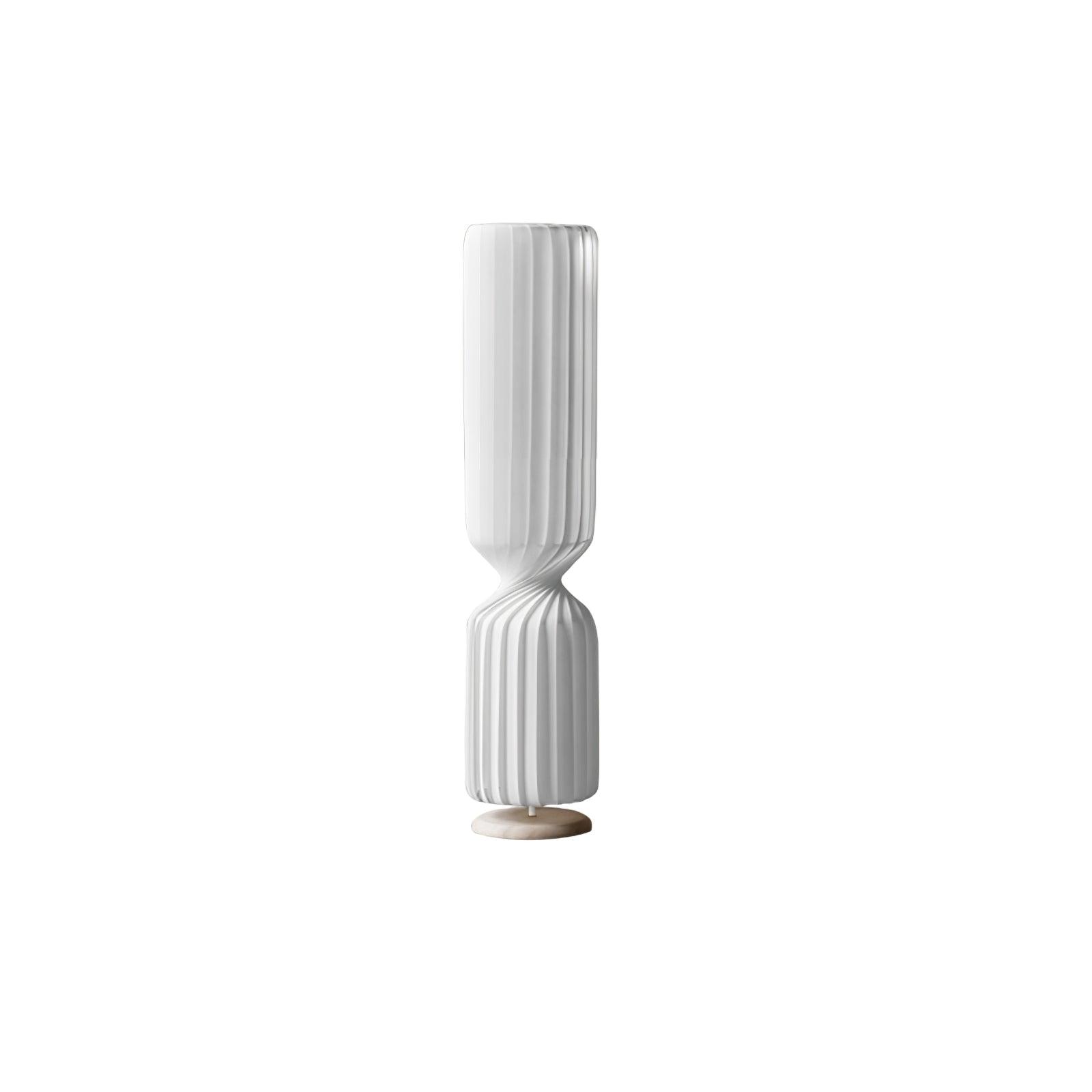 Short white Twist lamp on white background, with pleated upper and lower sections, narrow waist and pale round base