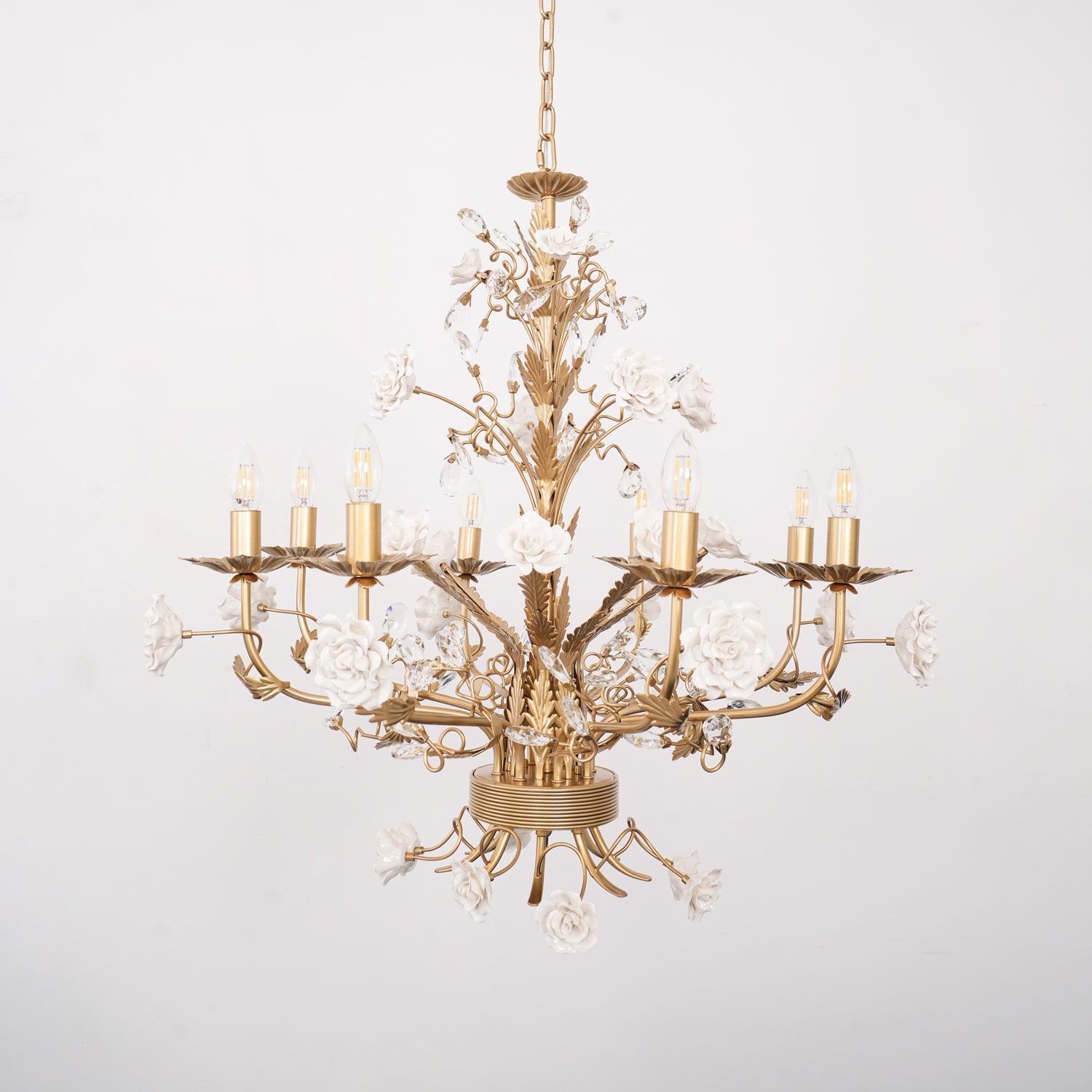 Frontal unlit eight-light White Rose chandelier against pale wall, with chain, golden leaf stem, crystal buds and lower roses