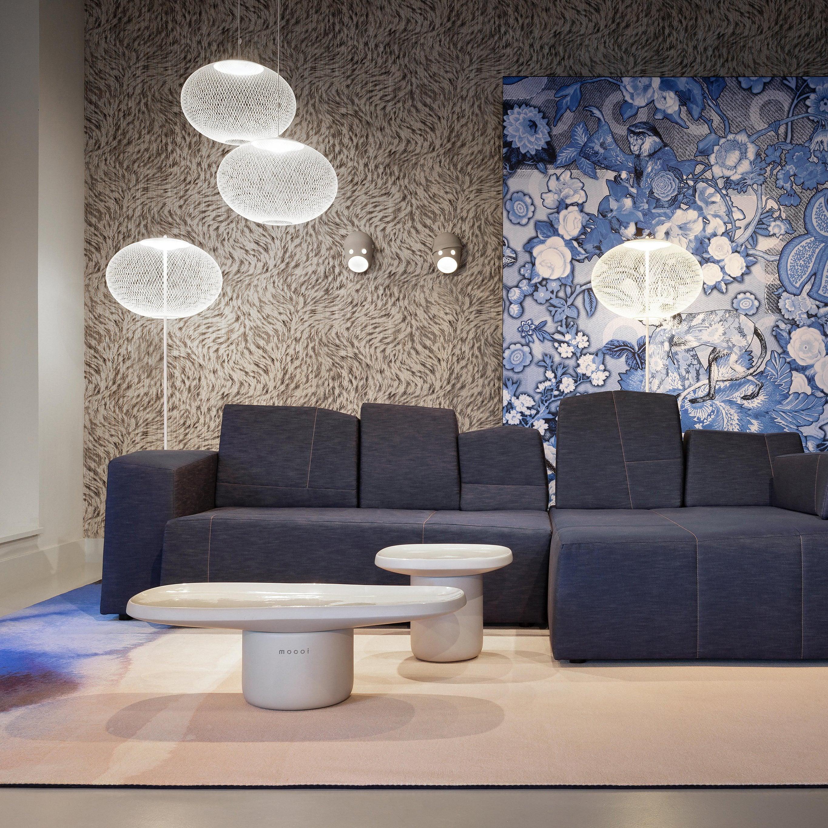 White mesh floor lamps beside a large dark sofa, with hanging mesh lamps, wall lights and blue floral artwork in the same room