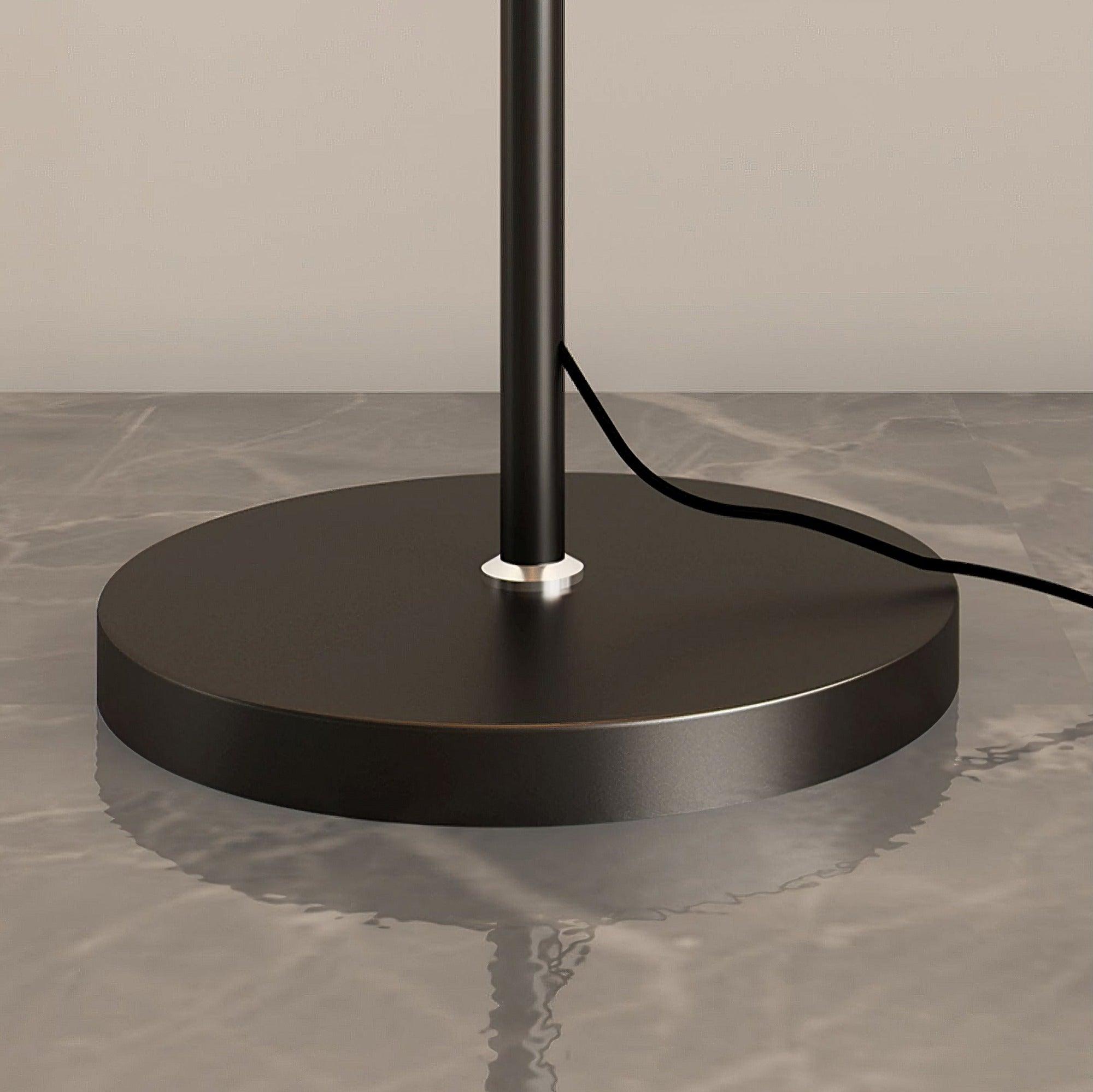 Low close view of a black circular base, slim stem, silver-looking collar and cord exiting above the base