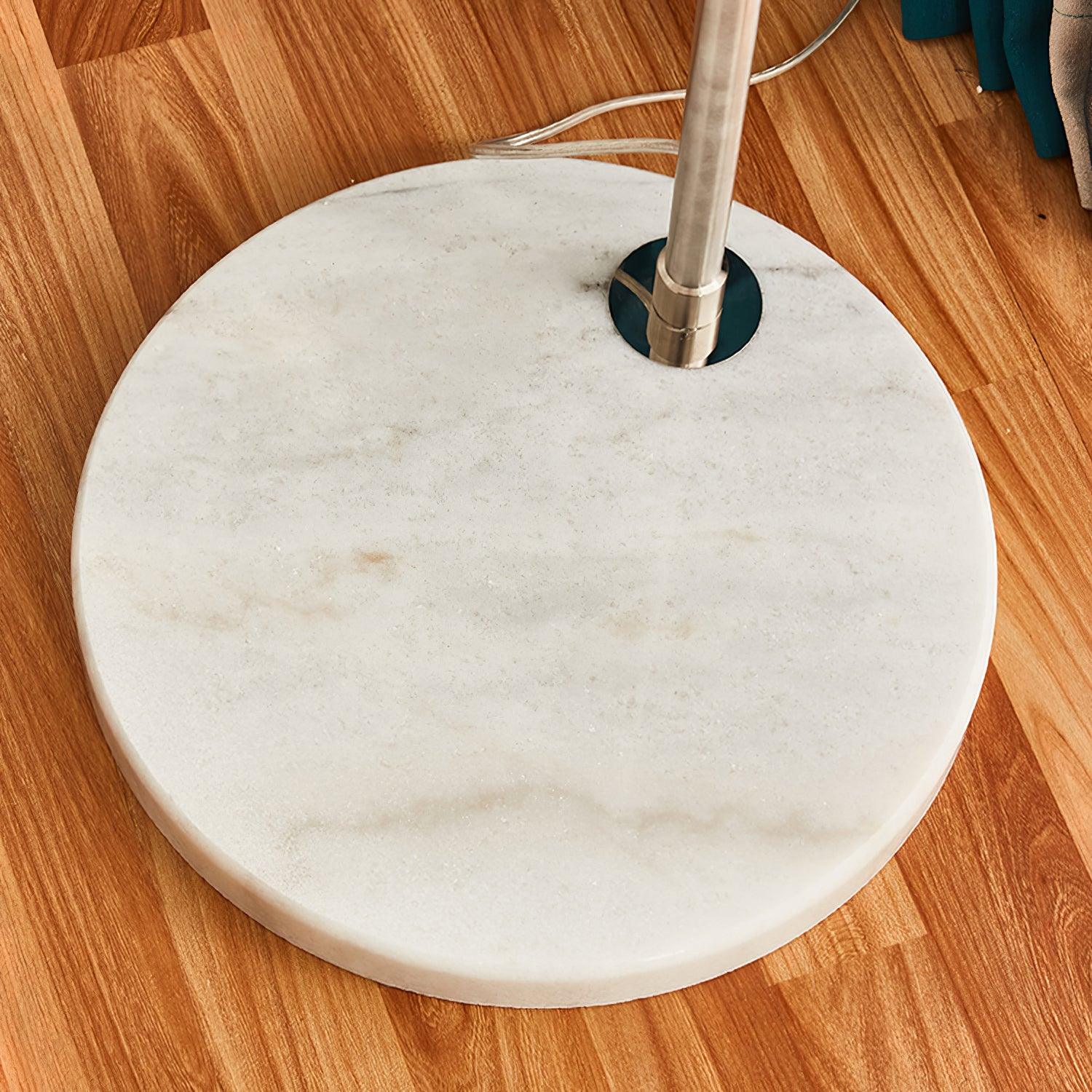 Close round pale marble base with natural markings, off-centre silver post and cable on wooden floor