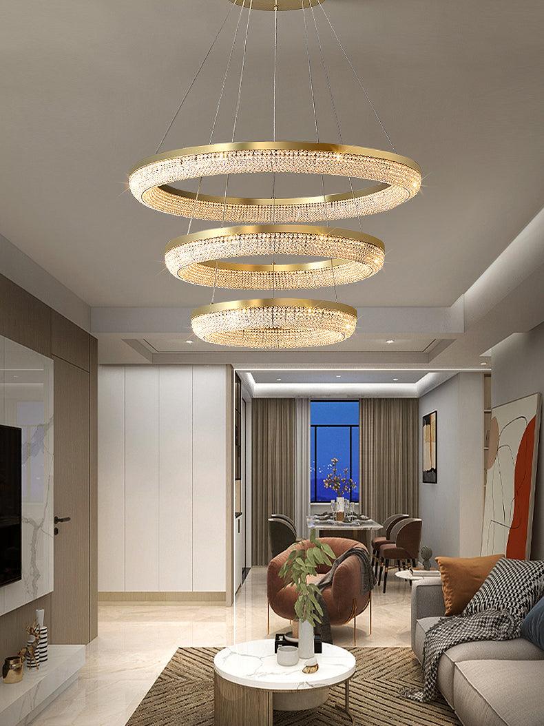 Three descending gold crystal rings in a living room with sofa and distant dining area