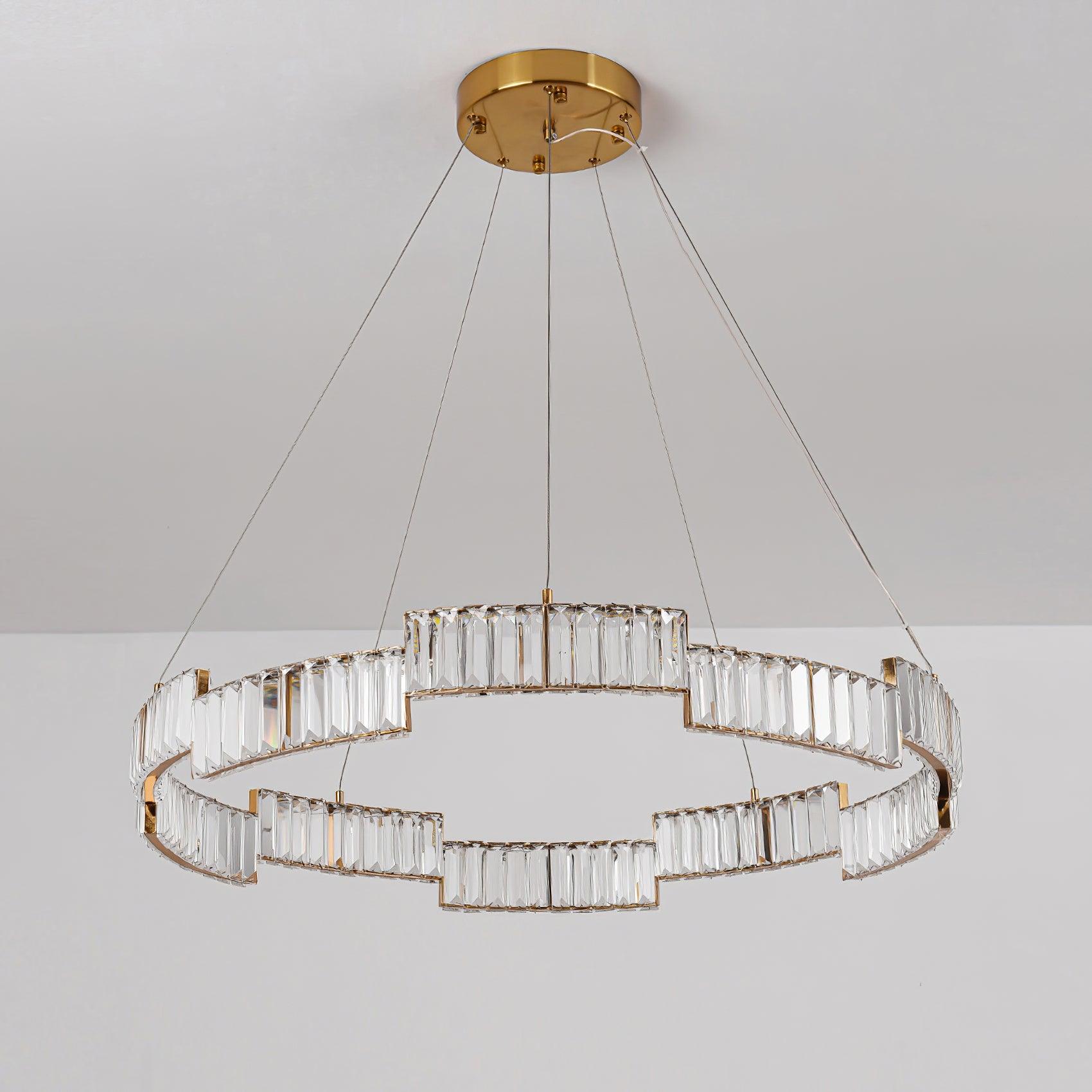 Unlit stepped ring chandelier with clear faceted panels, gold-tone rails, thin wires and round canopy on pale background