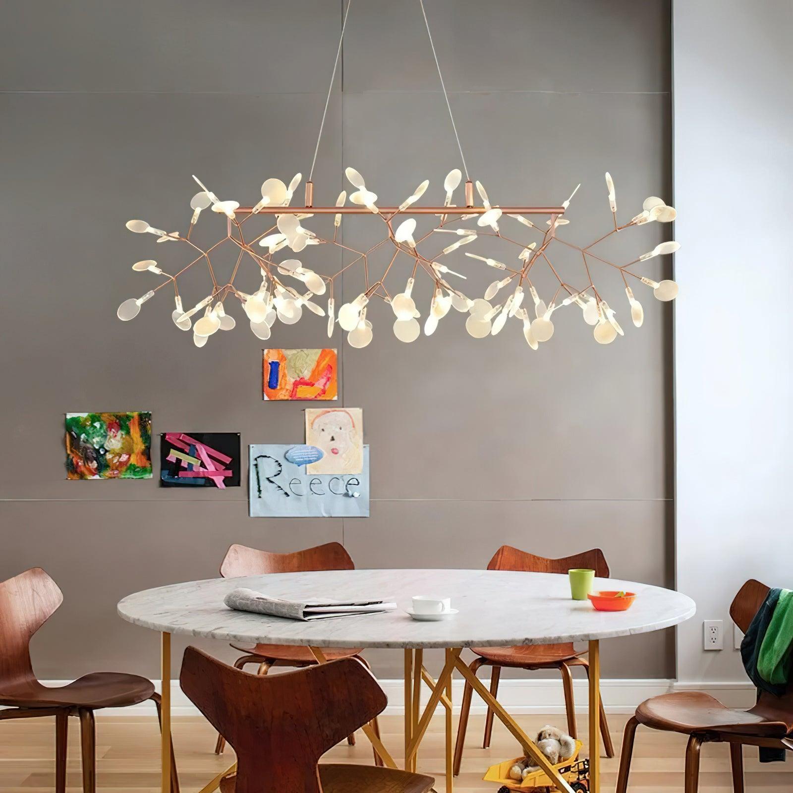 Branching chandelier above round pale stone table and wooden chairs, with small colourful pictures on grey wall