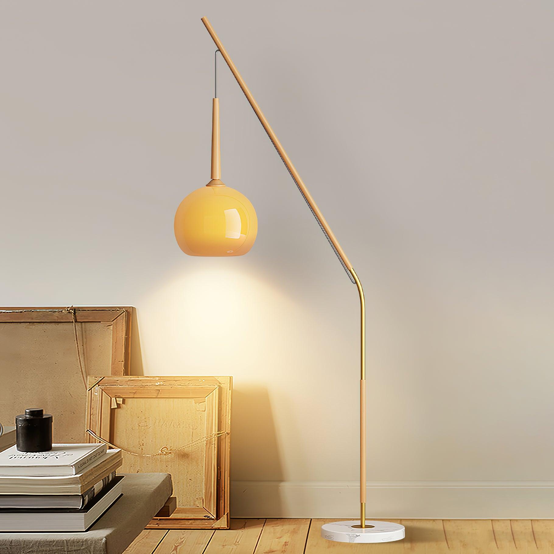 Orange hanging shade on a natural wood-colour floor lamp beside stacked picture frames and books on a bench