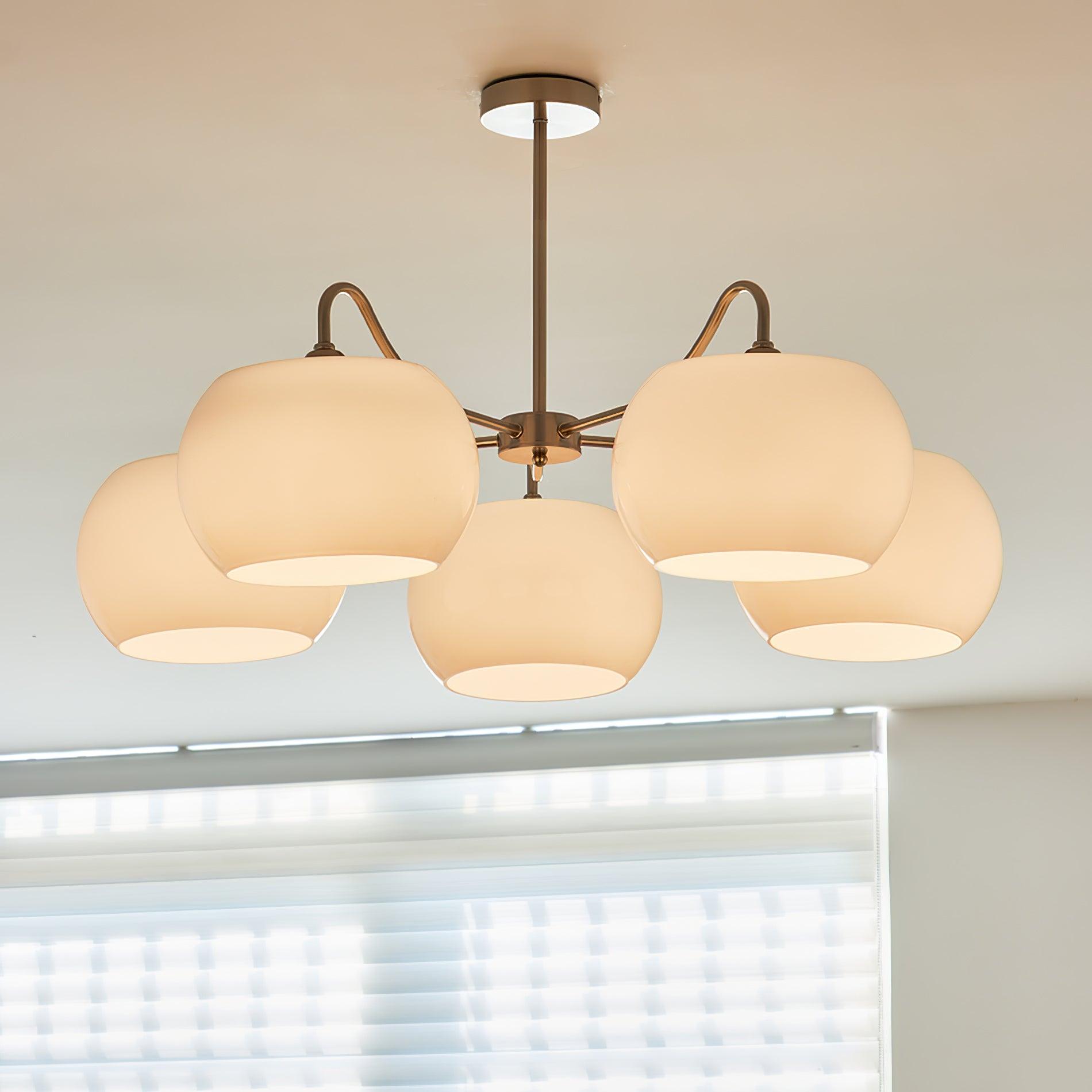 White glass chandelier with five open-bottom shades and a nickel-tone rod above window blinds