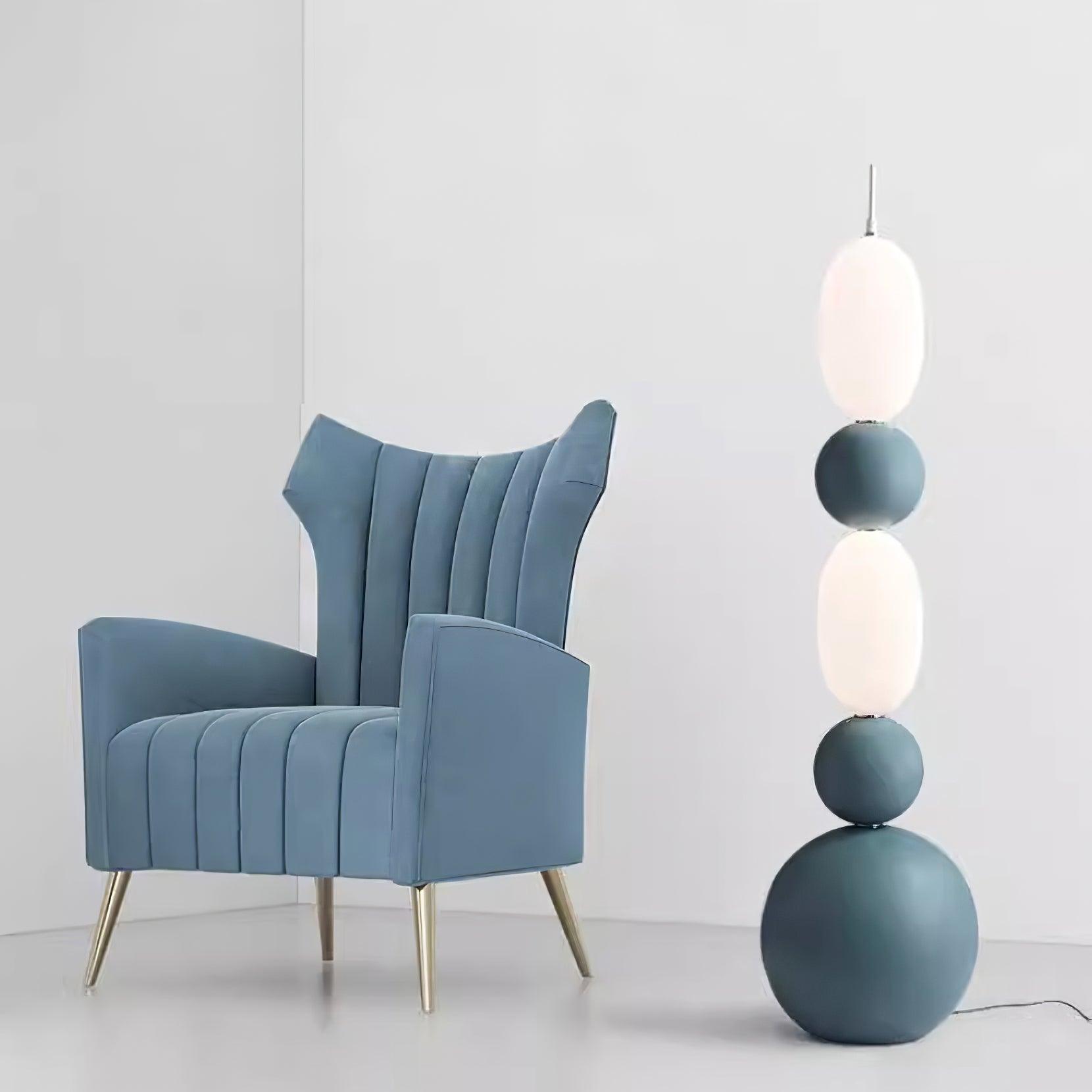 Blue stacked floor lamp with white oval shades and spherical details beside a blue pleated armchair