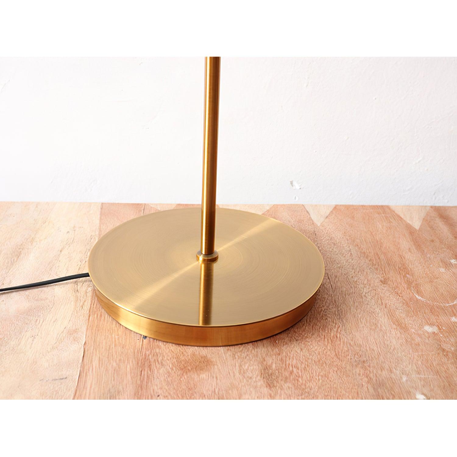 Close view of Kemi’s circular gold exterior base and stem on wood, with a black cord extending to the left