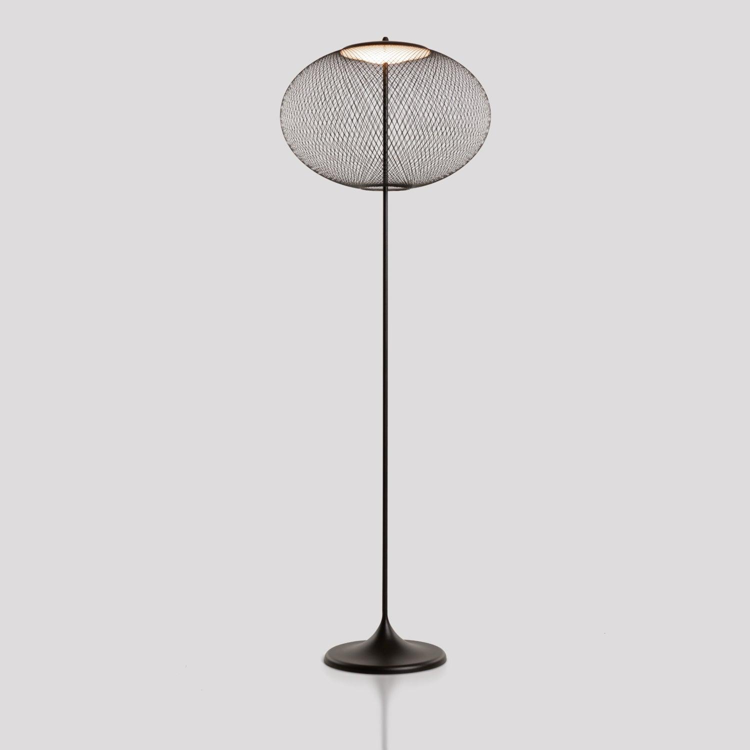 Black mesh floor lamp isolated against gray, with a rounded shade, narrow stem and flared base reflected below