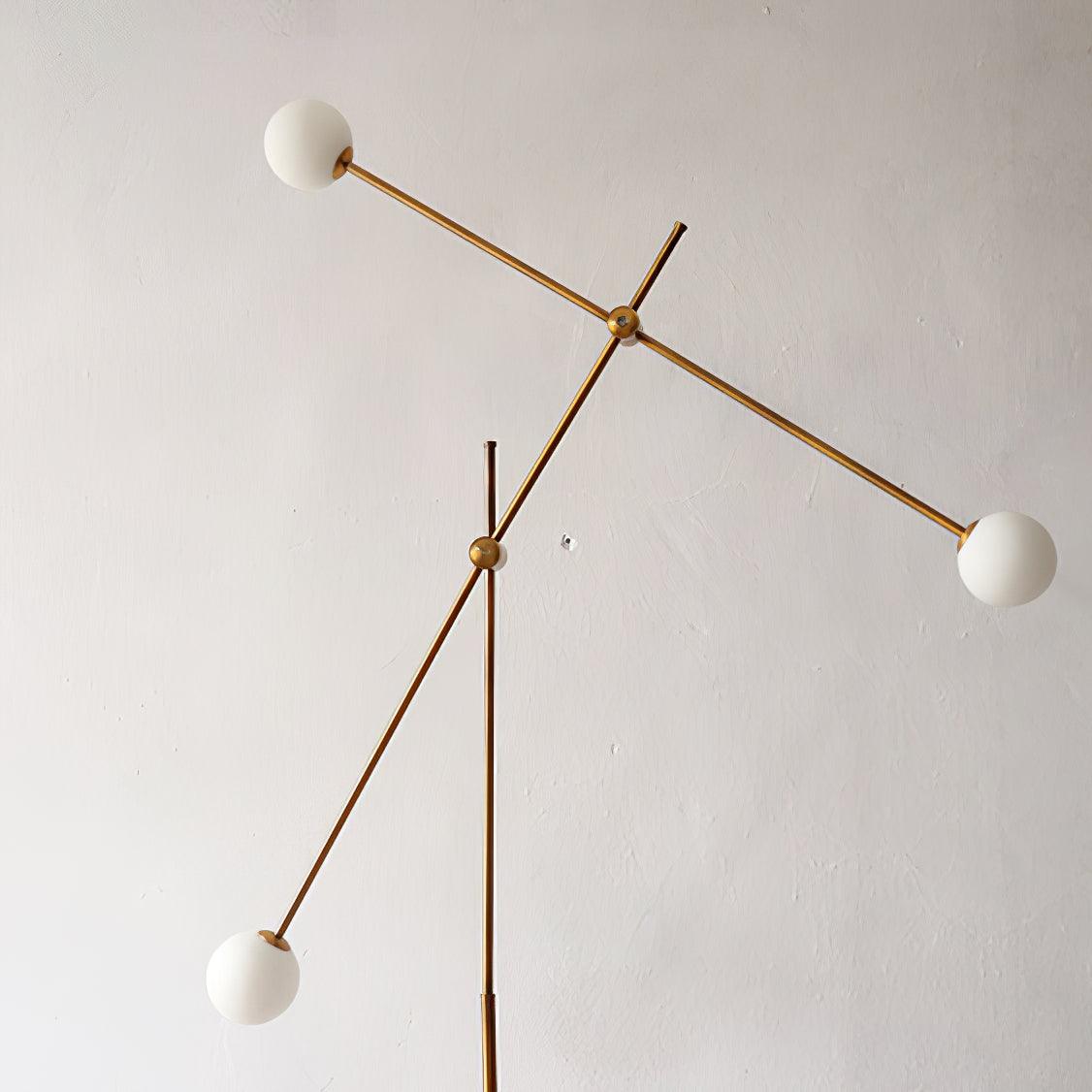 Close view of Kemi’s unlit white globes, crossing gold rods and round joints against a pale plaster wall