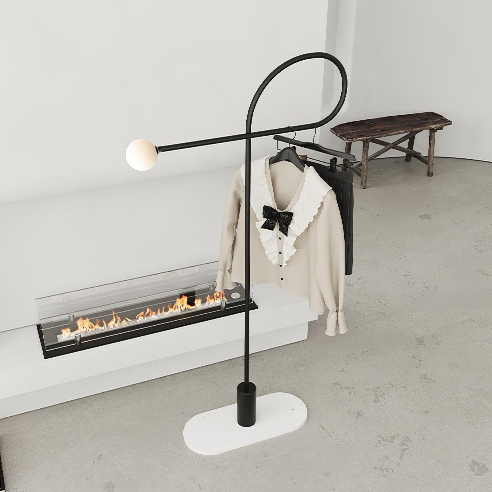 Angled view of the black loop lamp with a white globe, blouse and skirt on hangers and white oval plate beneath its base