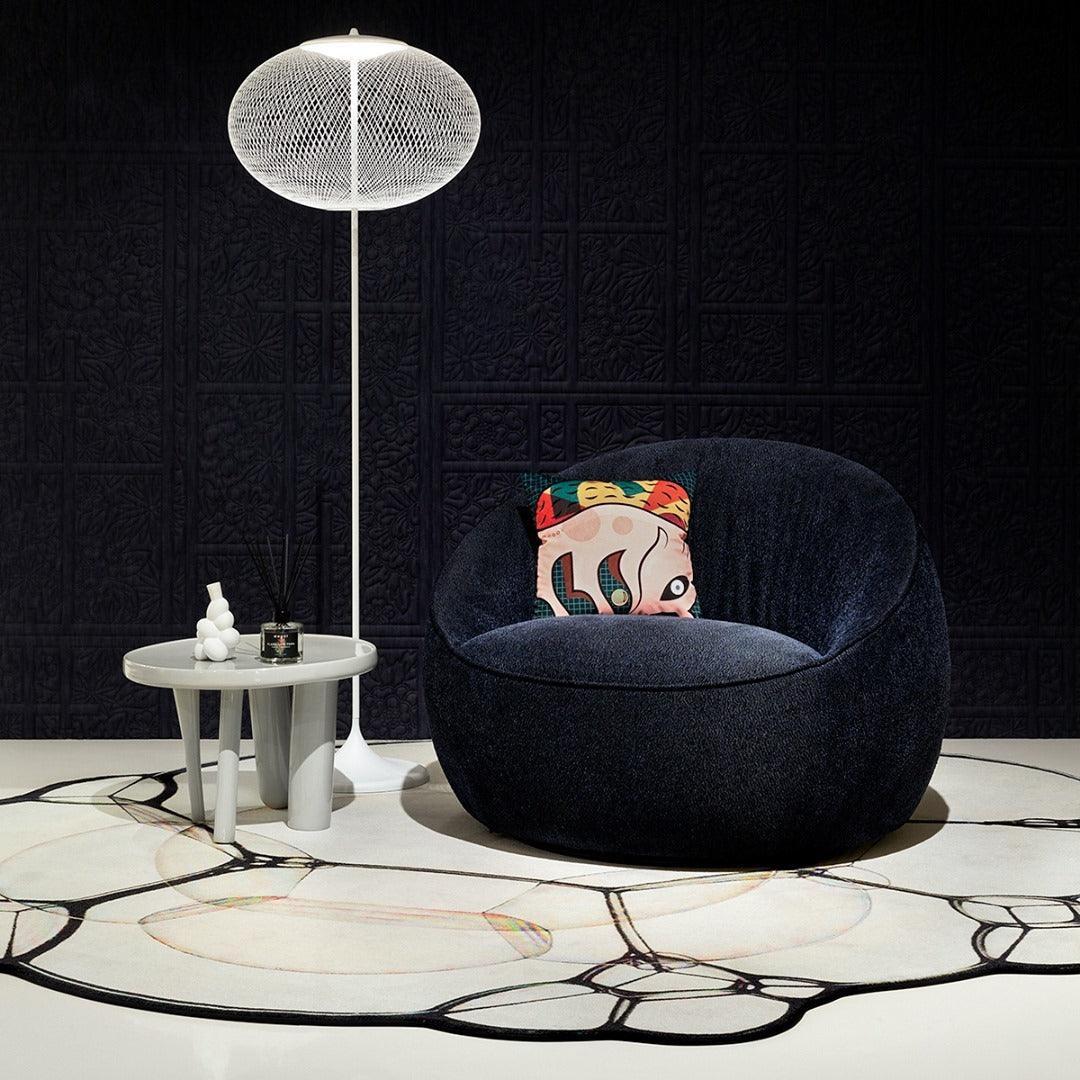 White mesh floor lamp beside a dark rounded chair, white side table and patterned rug against a black textured wall