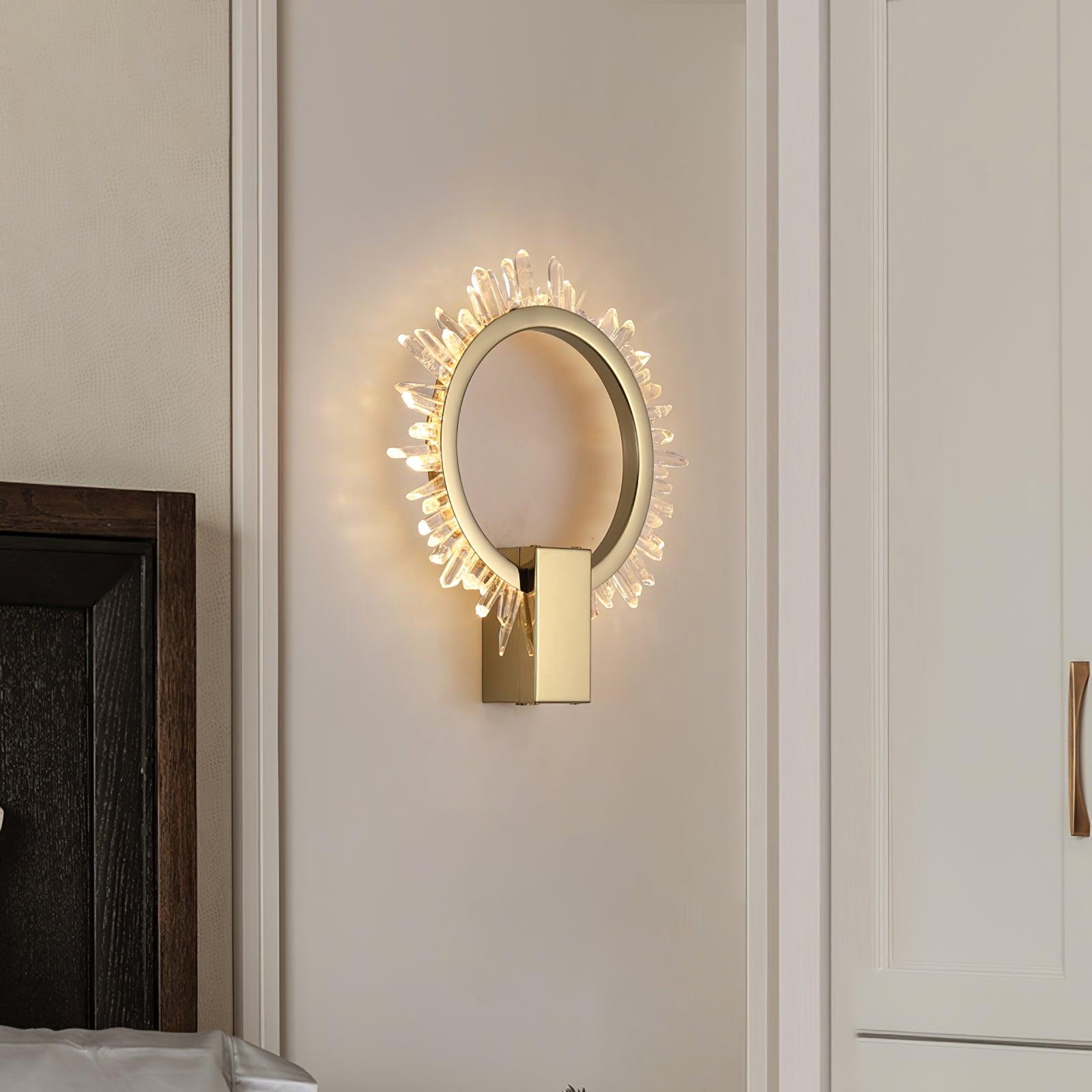 Angled lit gold crystal ring wall light on pale panelling beside a wardrobe and bed edge