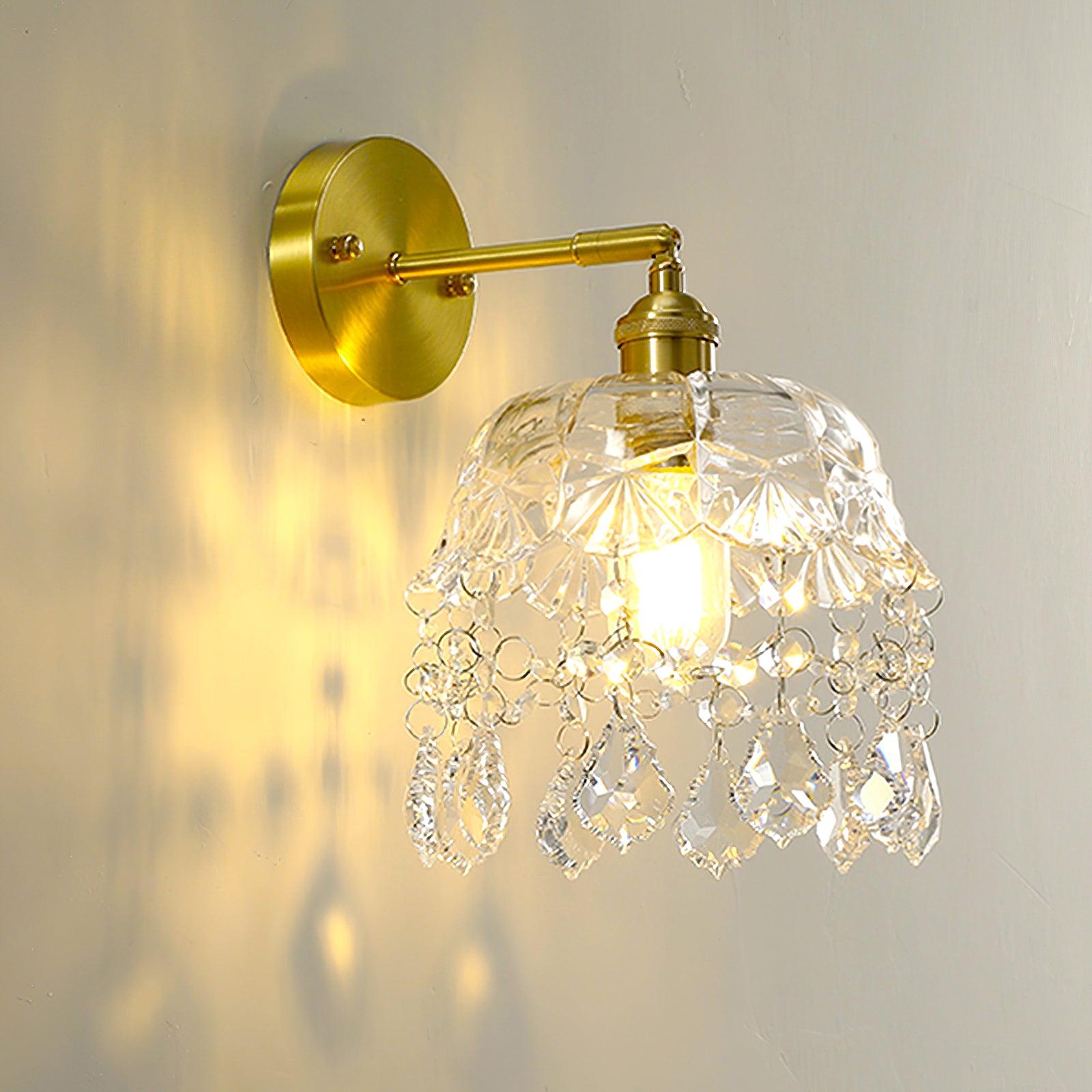 Close lit patterned clear bell and faceted drop fringe below a gold-tone arm and round wall plate