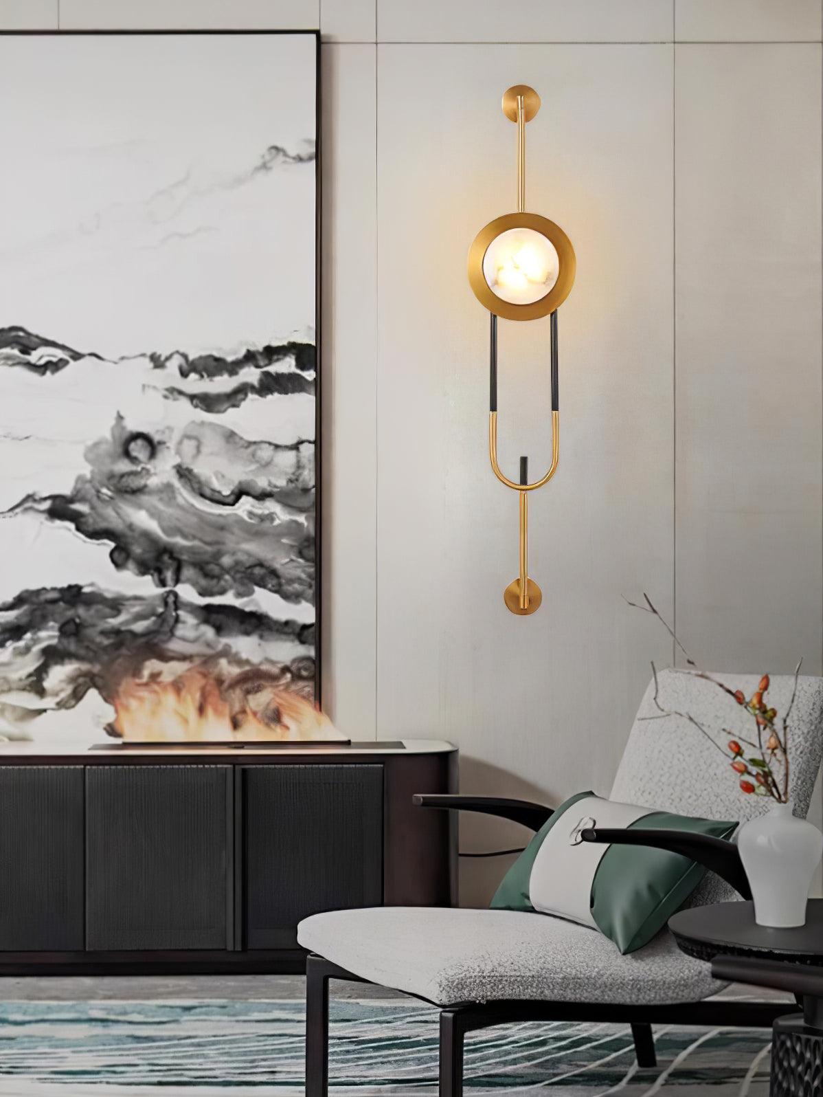 Lit marble and gold wall light beside landscape artwork, a chair and a decorative fire console