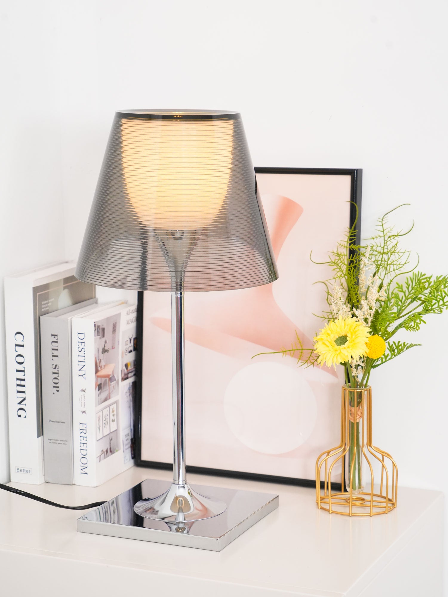 Chrome Prism table lamp on a pale surface beside a flower vase