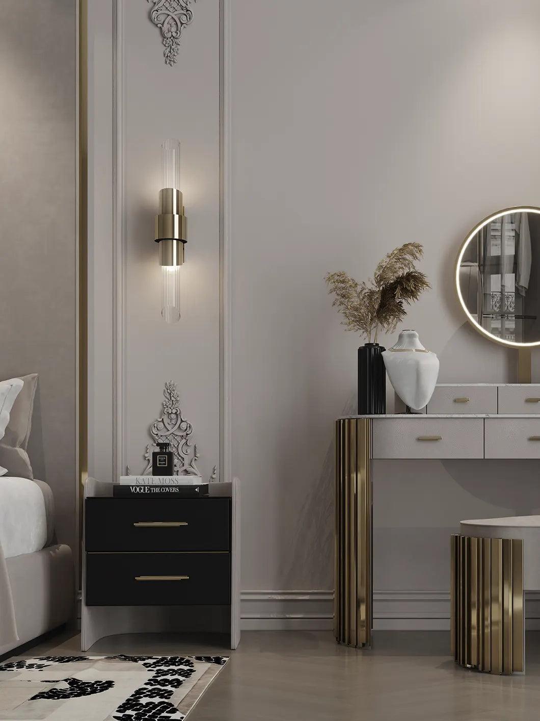 Closer bedside view of crystal wall light in ornate panel above black nightstand, beside vanity and partially shown lit mirror