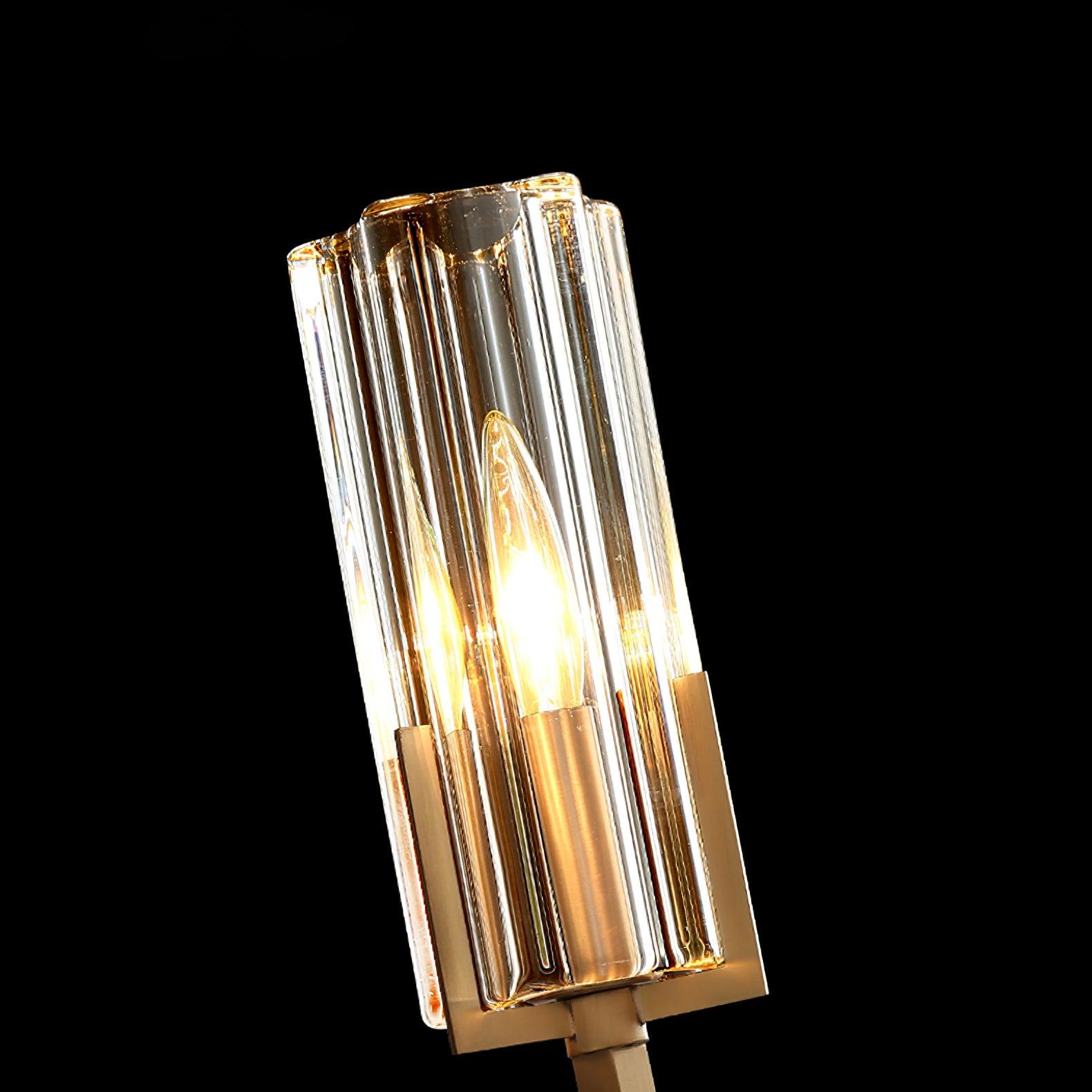 Close upper clear fluted glass cylinder around lit candle-shaped bulb on black background, with brass support at lower edge