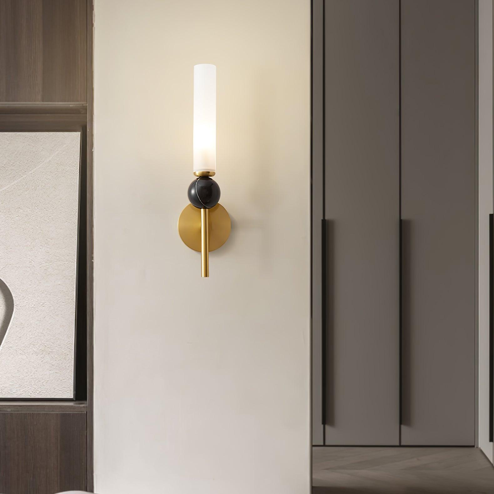 Wider bedroom view of straight brass marble wall light with lit cylindrical diffuser, round plate and closet beyond