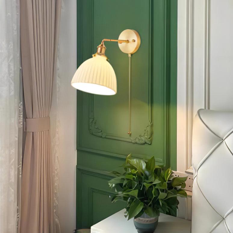 White pleated wall light on green moulded panelling beside a white padded headboard, curtain and plant