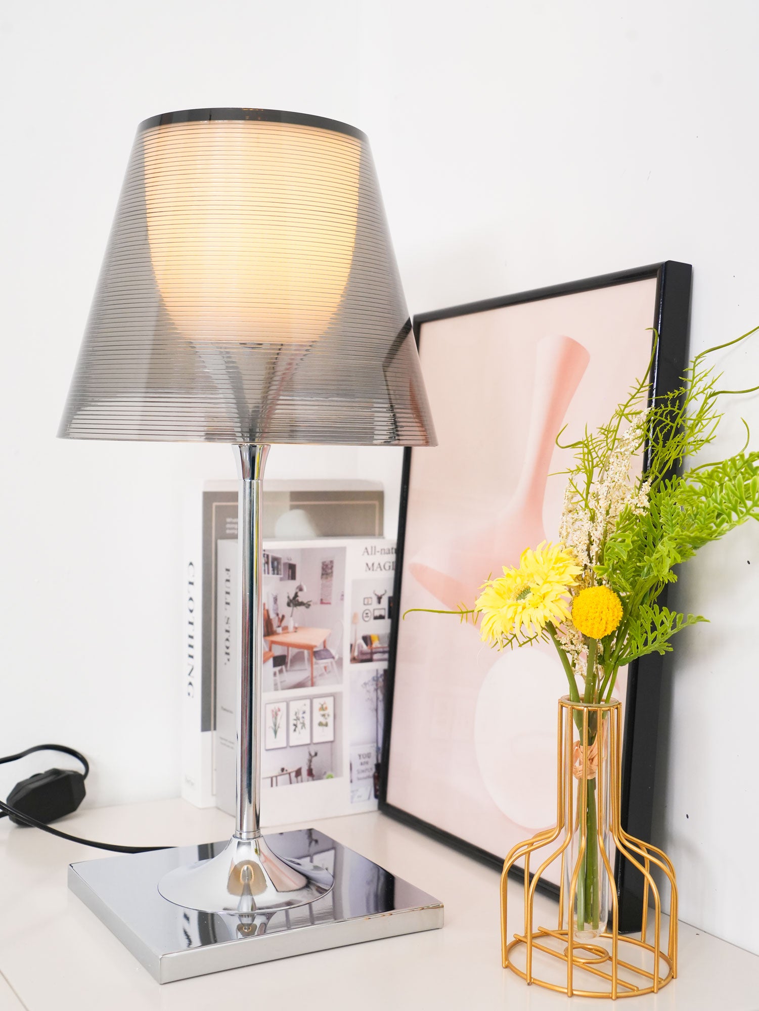 Chrome Prism shade lit beside books and yellow flowers