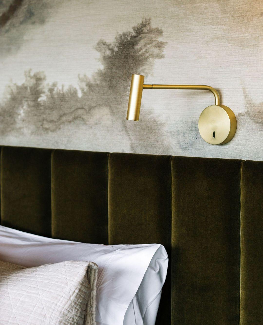 Gold wall light beside an upholstered bed