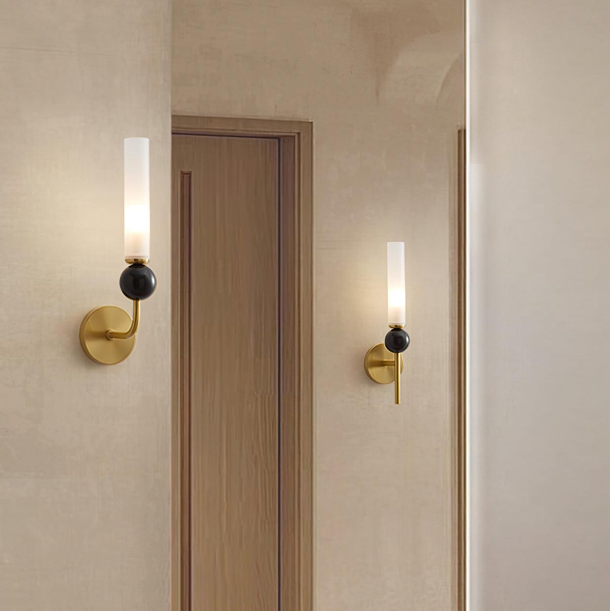 Brass curved-arm marble wall light beside tall mirror, with a straight-stem light reflected in the glass