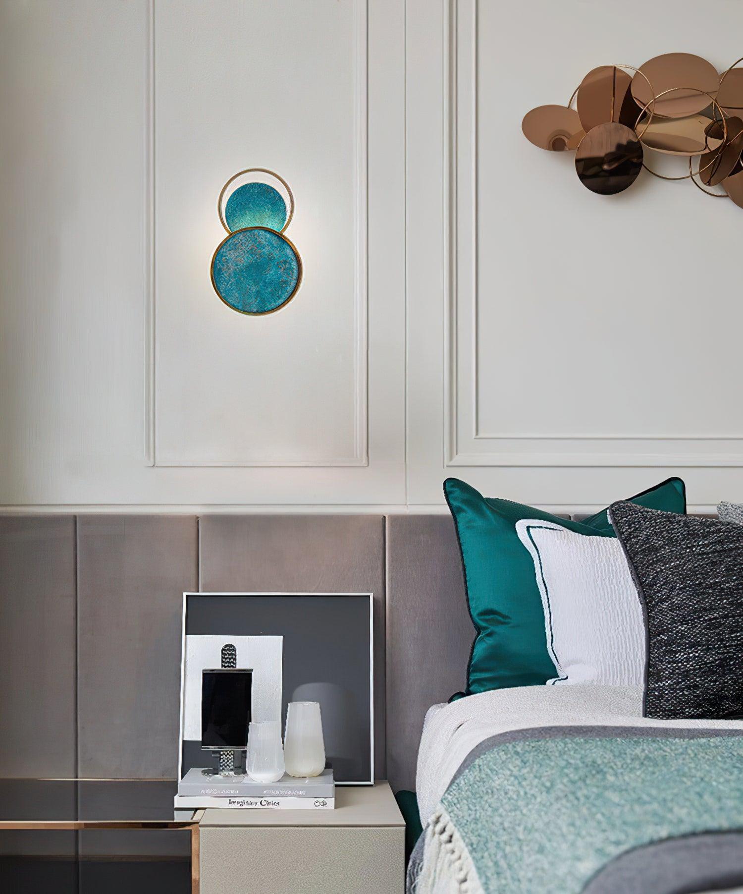 Single turquoise wall light on white panelling above a sofa with teal cushions, beside another circular wall decoration.