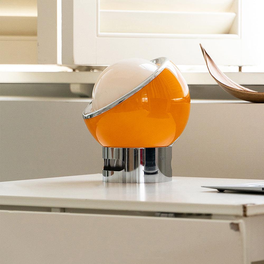Orange-toned Valeria glass lamp on a desk beside white window shutters
