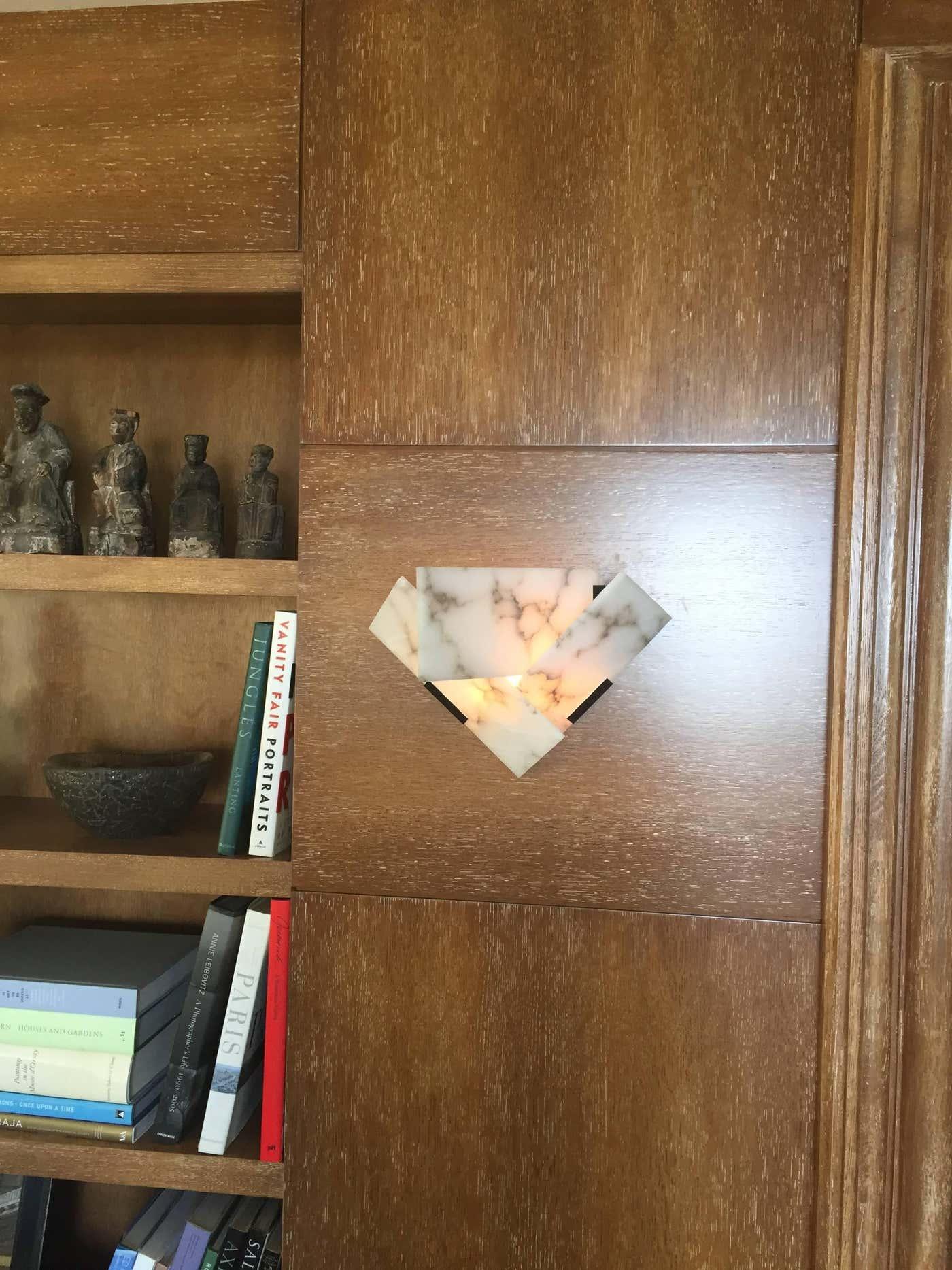 Lit veined alabaster wall sconce on wood paneling beside shelves with books and figurines