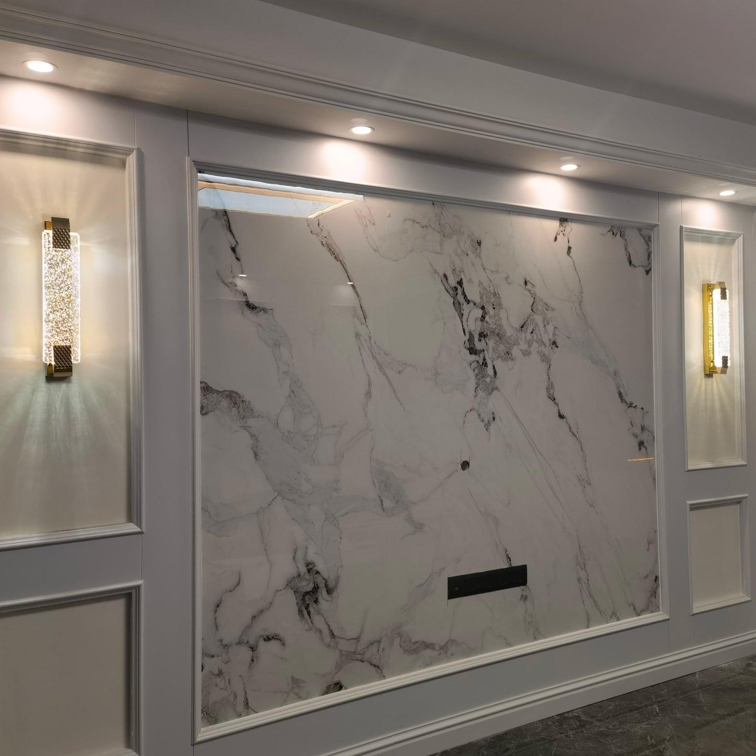 Two illuminated Moet wall lights framing a broad marble-look feature wall with white panel molding and ceiling spotlights