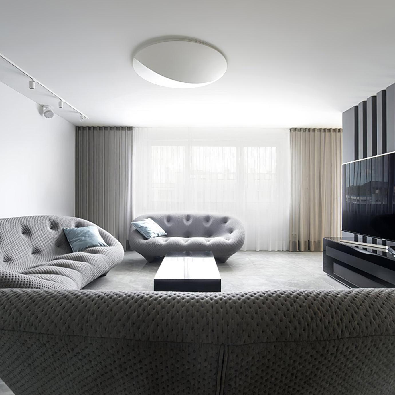Circular white fixture pictured on a living-room ceiling above grey sofas, with track lights and a television nearby