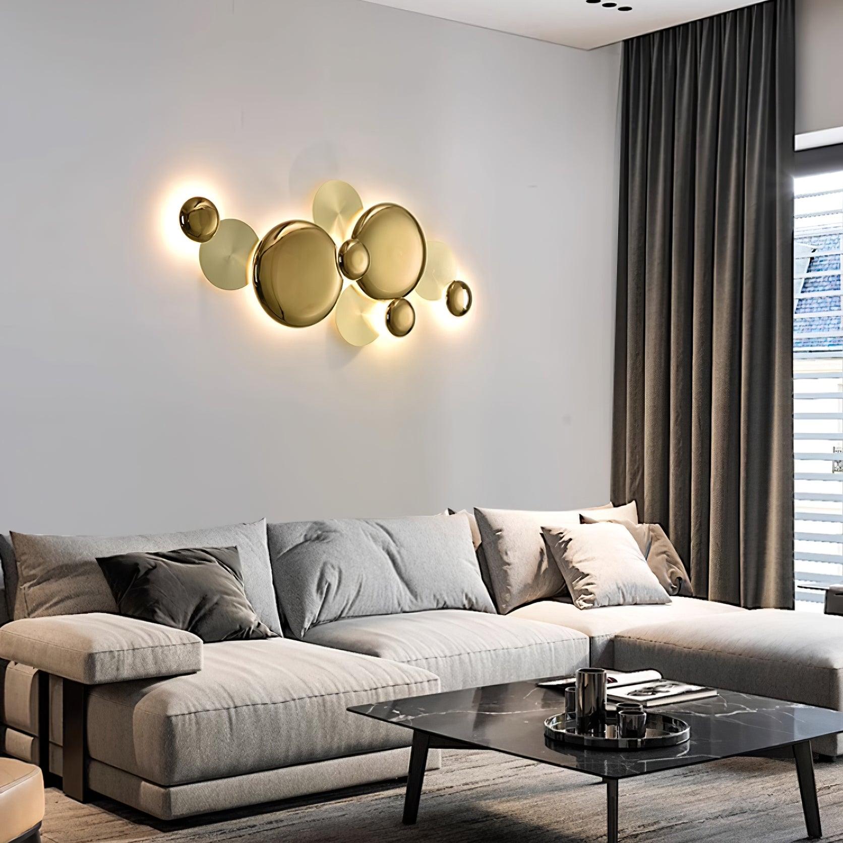Lit gold disc wall lamp above a pale sectional sofa beside dark curtains and a black coffee table