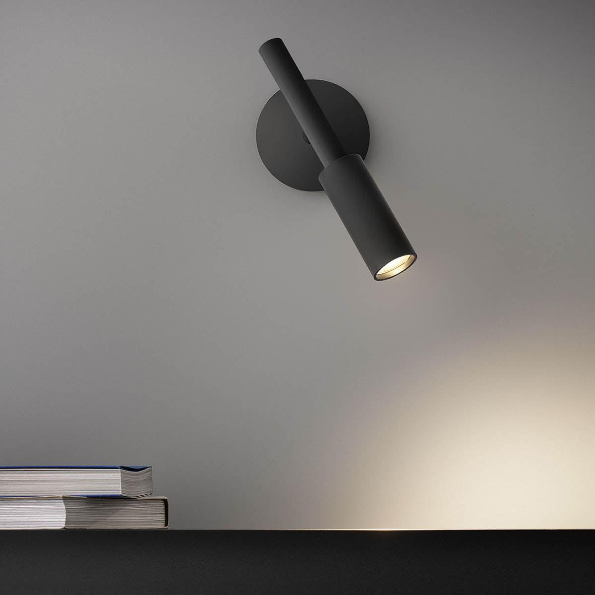 Black Tubino wall light angled above a surface with stacked books
