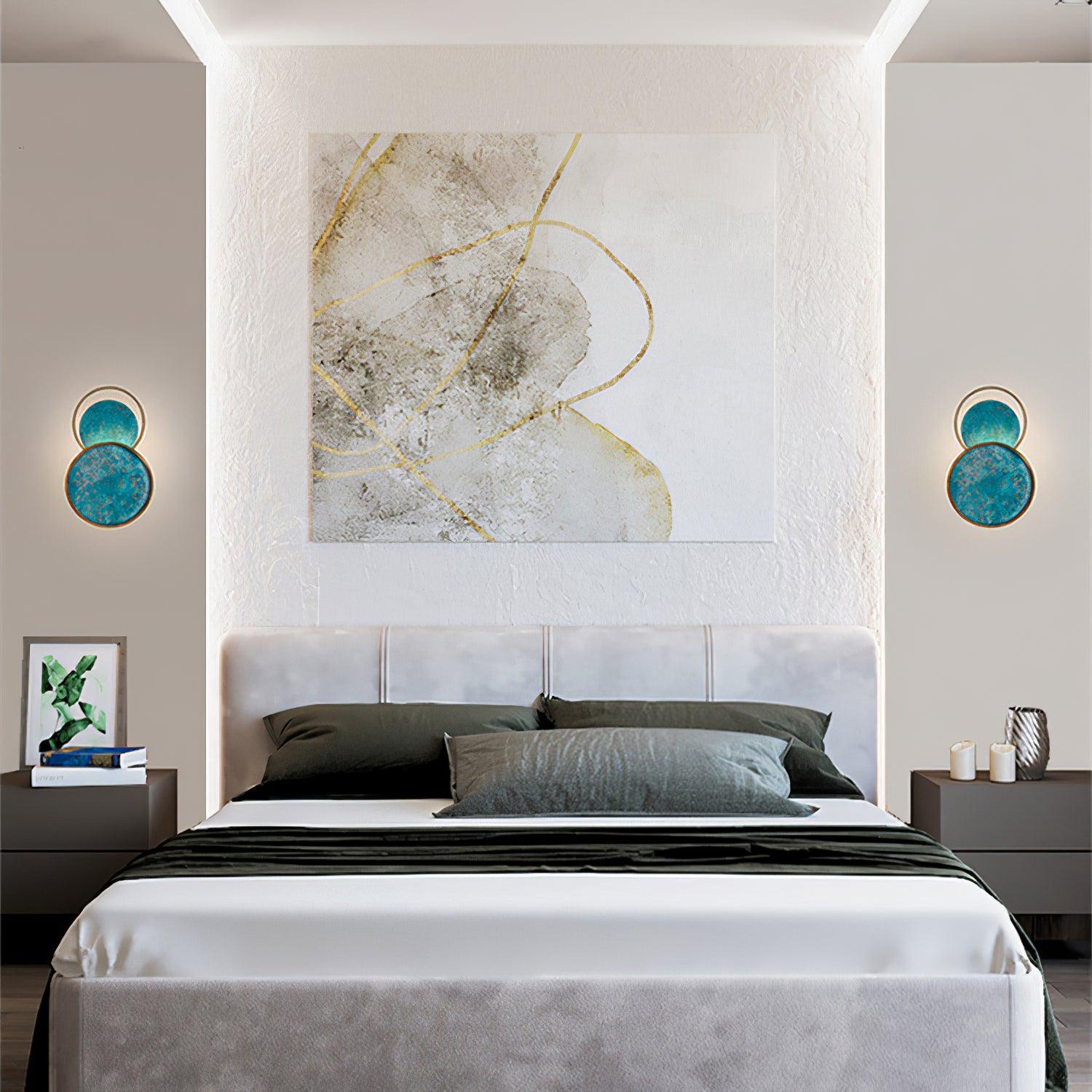 Paired blue circular wall lights above bedside cabinets, beside a padded headboard and large abstract artwork.