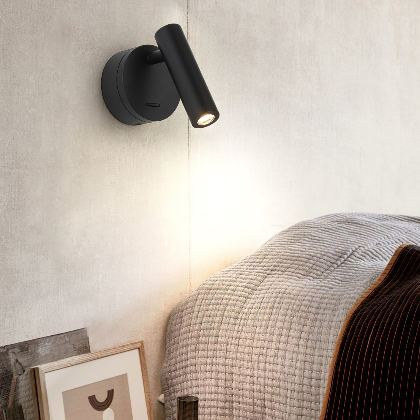 Black cylindrical lamp above a bedside picture