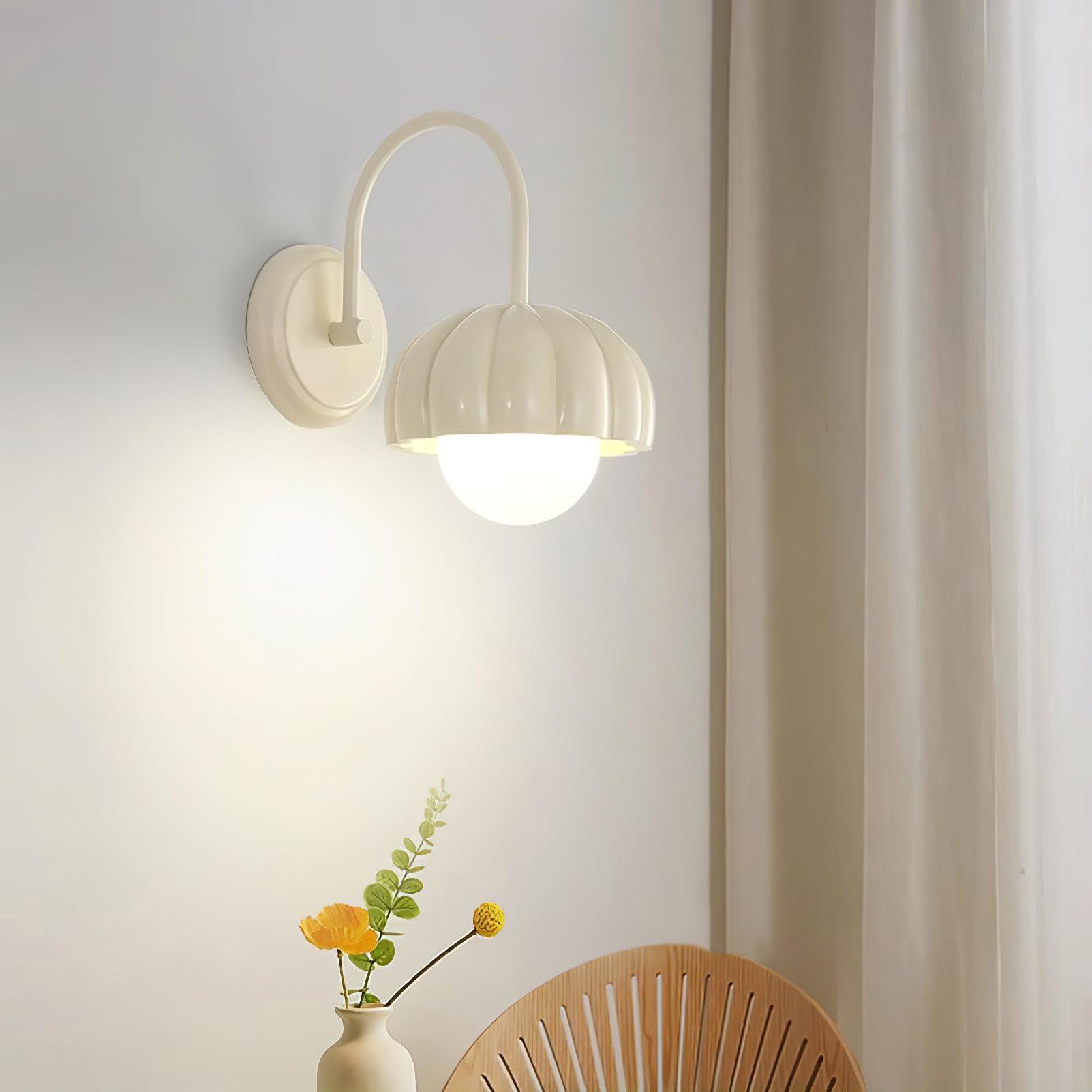 Illuminated cream pumpkin wall light above a flower vase and wooden chair near a curtain