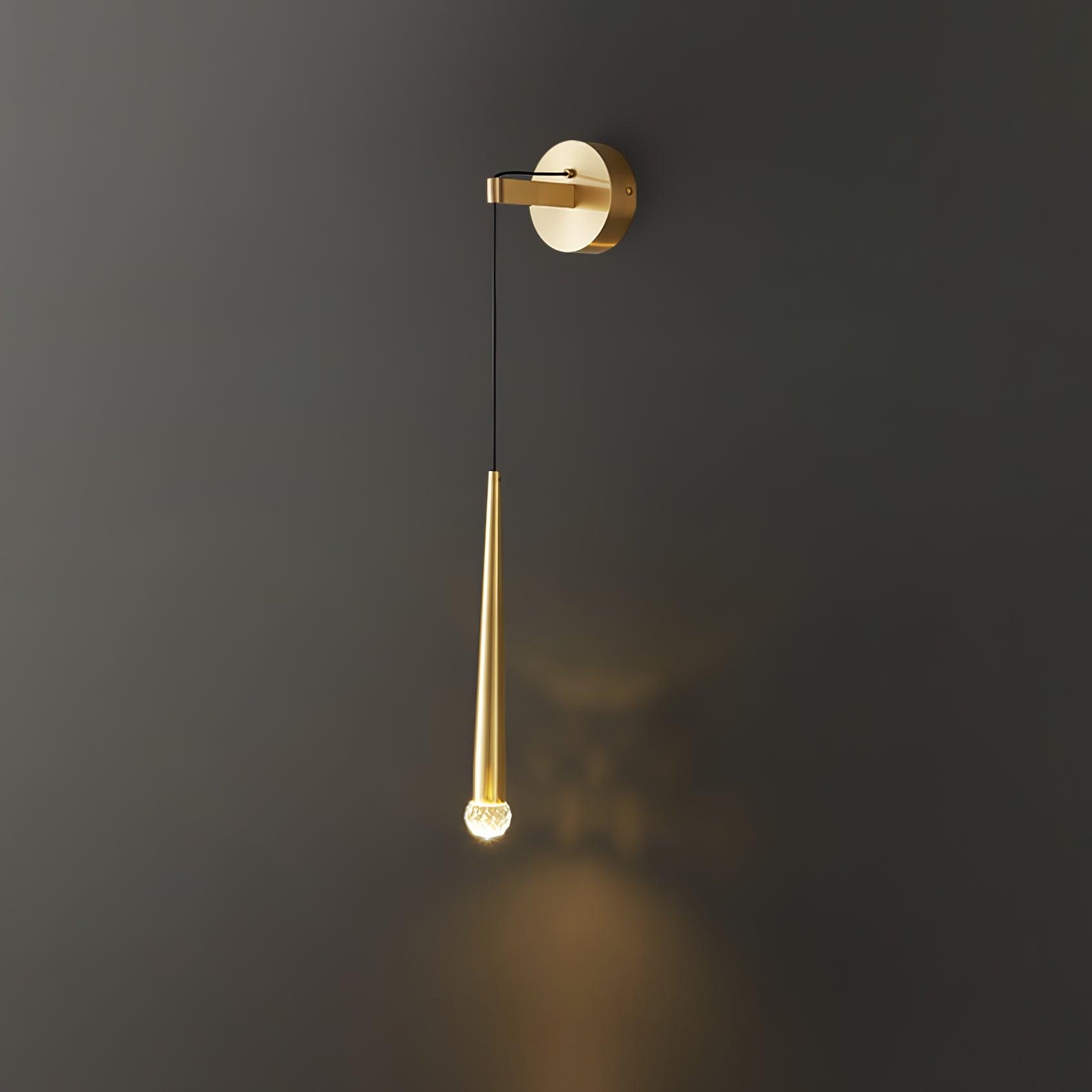 Brass-tone crystal-tipped conical wall light lit against dark grey, with a pattern around the lower tip